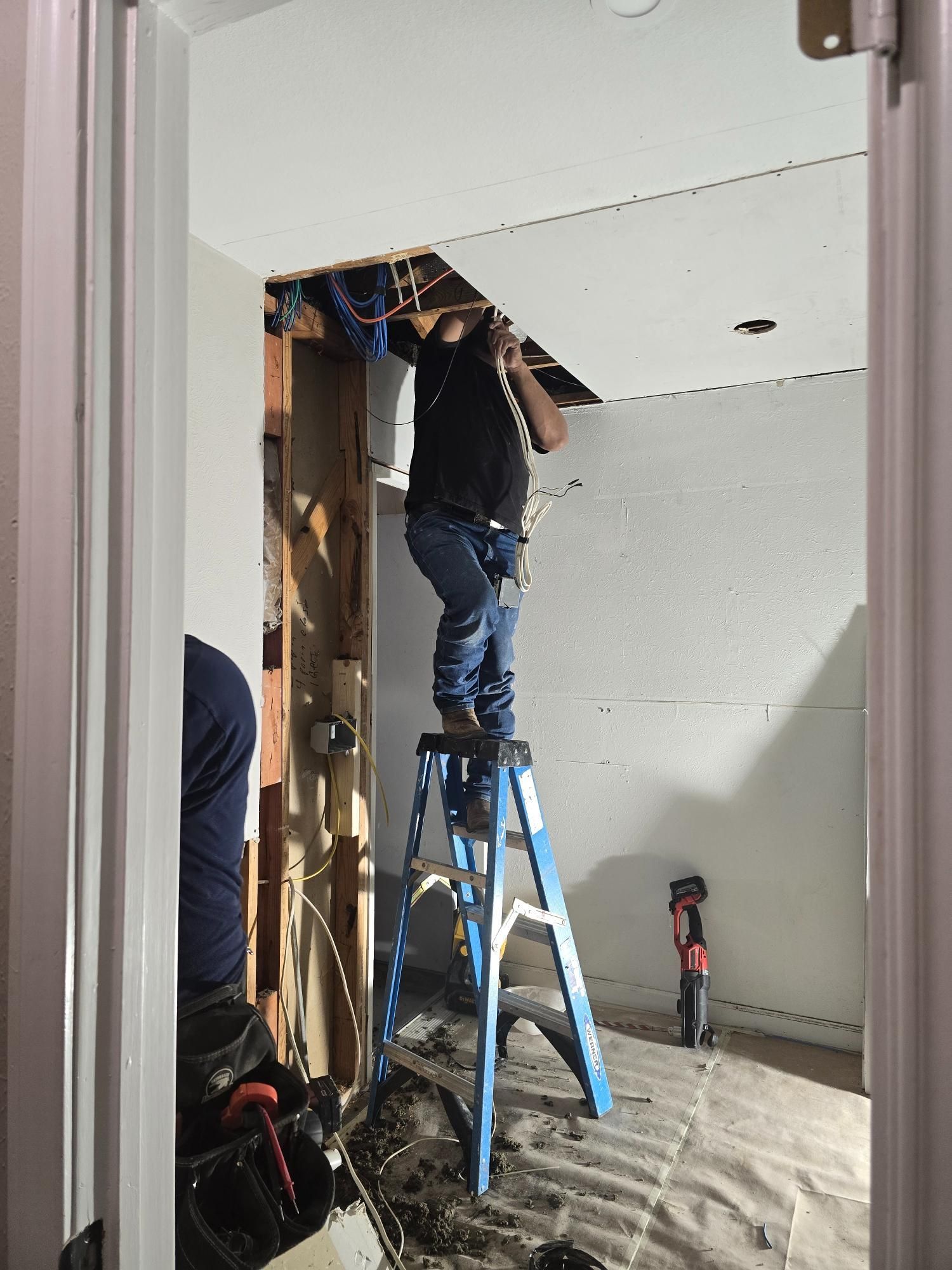 Man on stepladder repairs ceiling, another person on left. Bathroom under renovation.