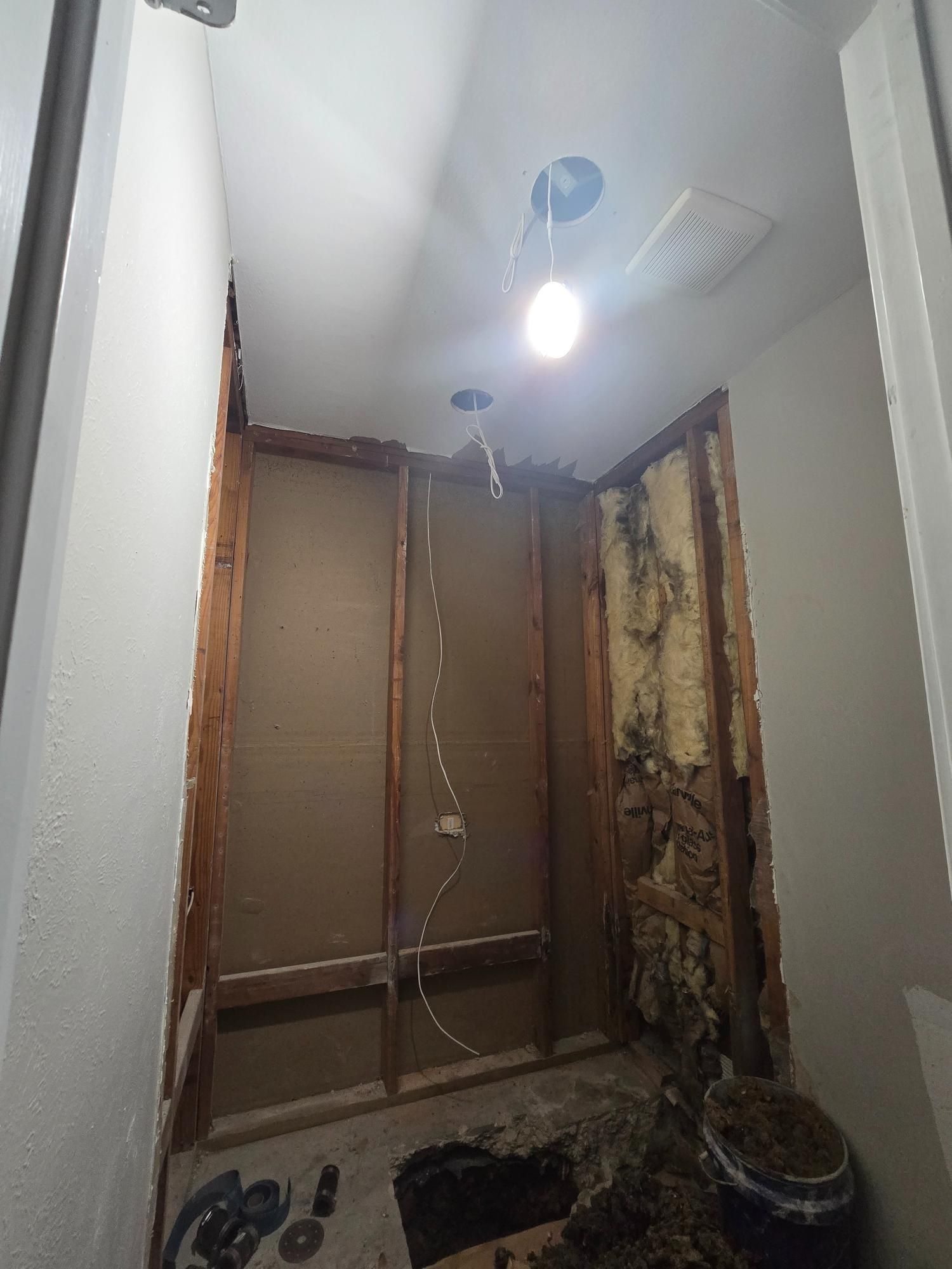 Bathroom under construction, walls open to studs, overhead light illuminates space.