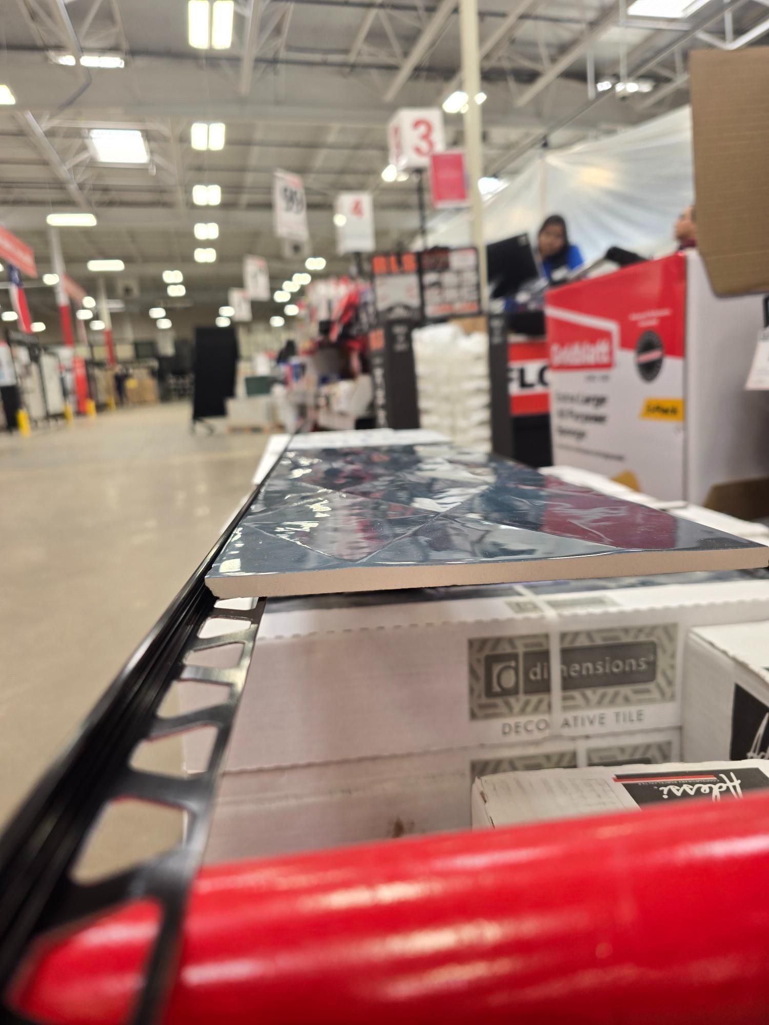 Tiles in a shopping cart at a home improvement store, with blurred background of aisles and staff.