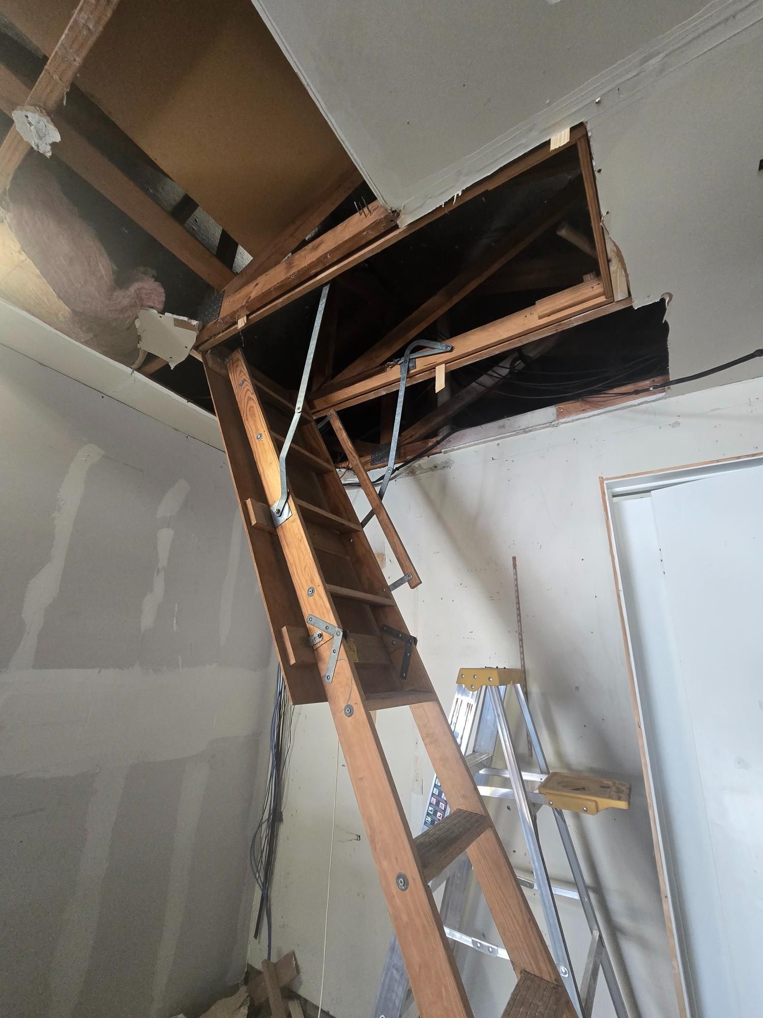 Wooden attic ladder extending from ceiling opening; silver stepladder nearby.