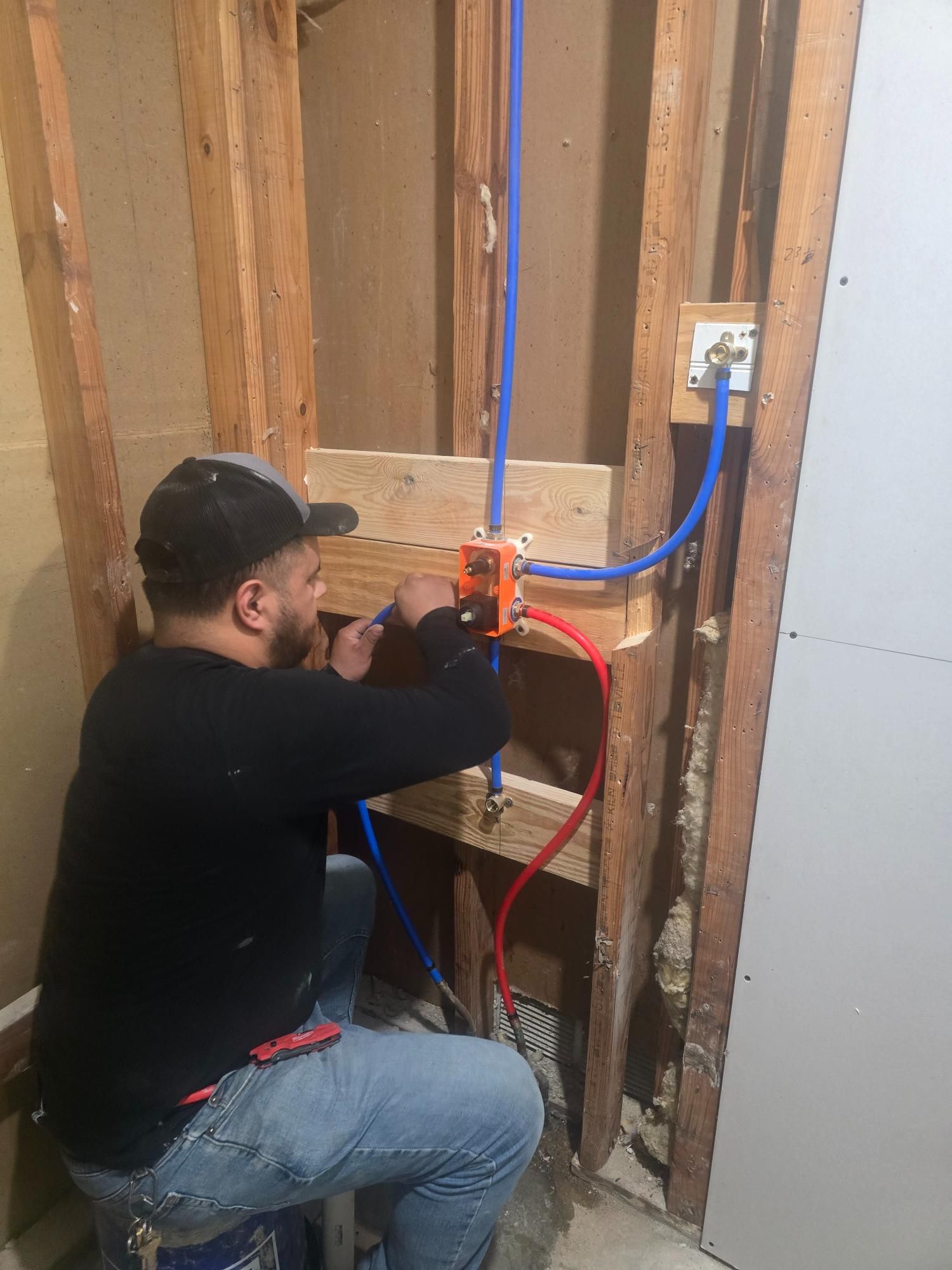 Plumber installing pipes in a wall cavity, using blue and red PEX tubing.