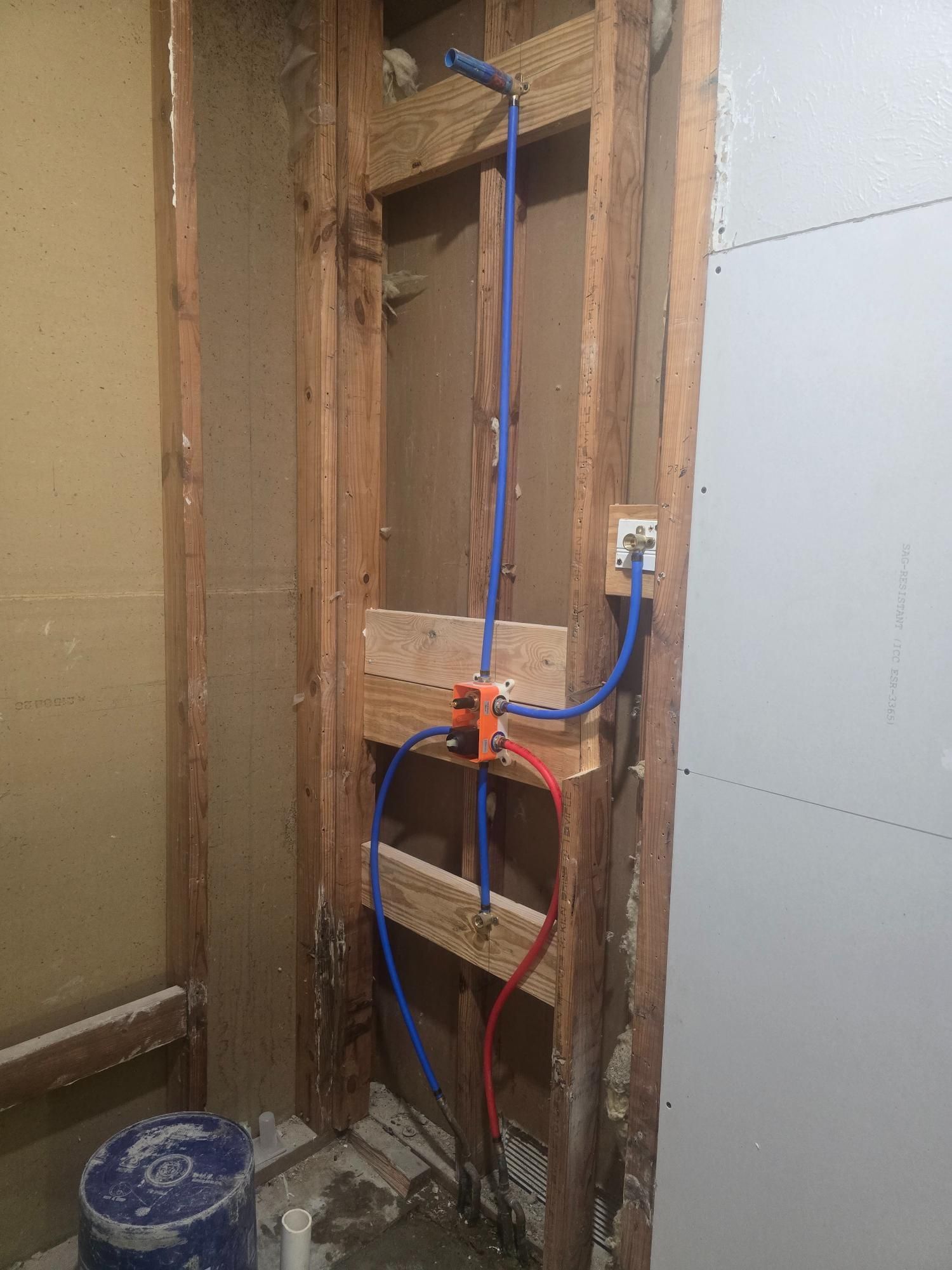 Bathroom wall frame with blue and red water pipes, shower valve, and electrical outlet.