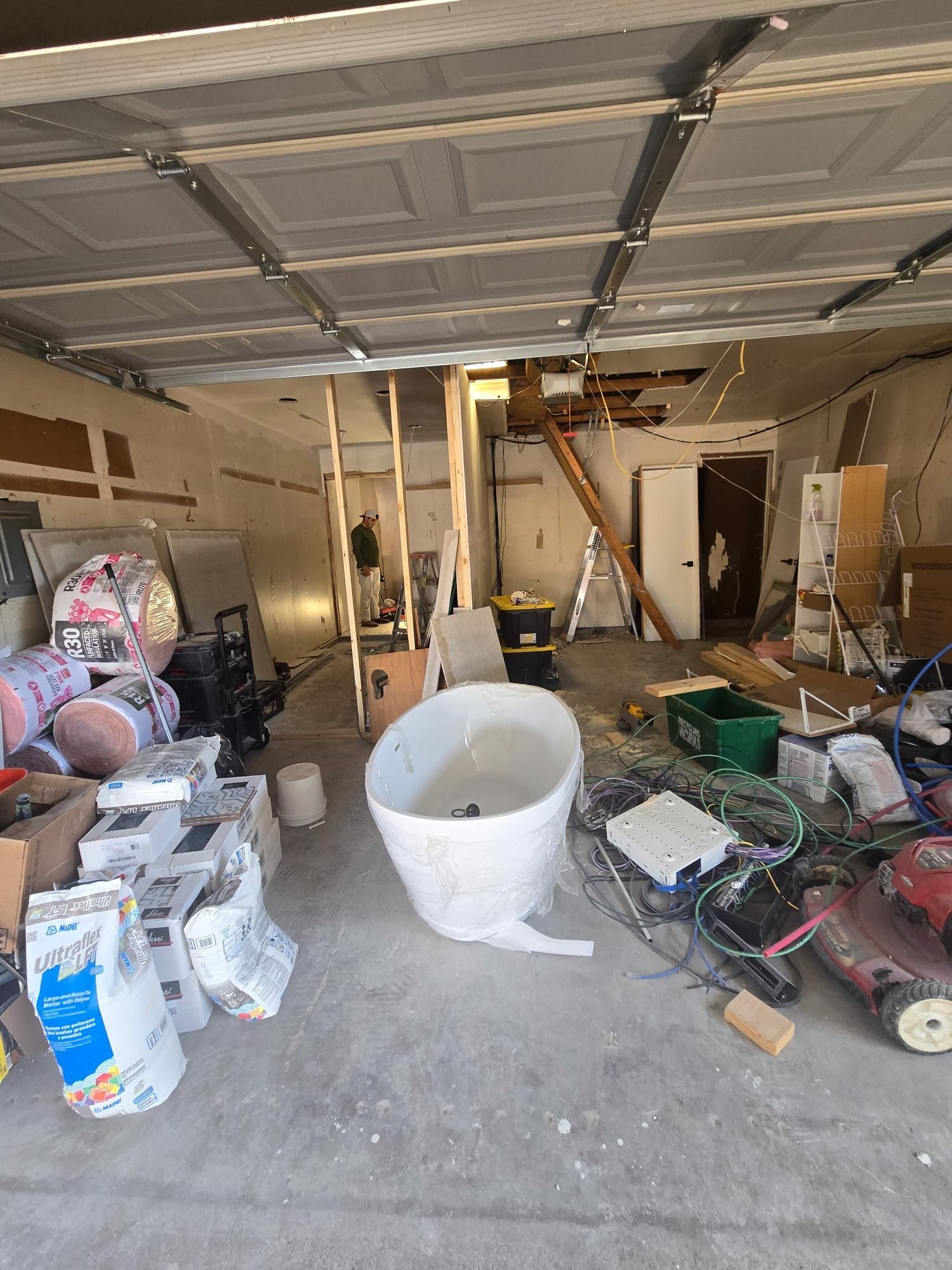 Garage interior with construction materials and debris; a ladder leads up.