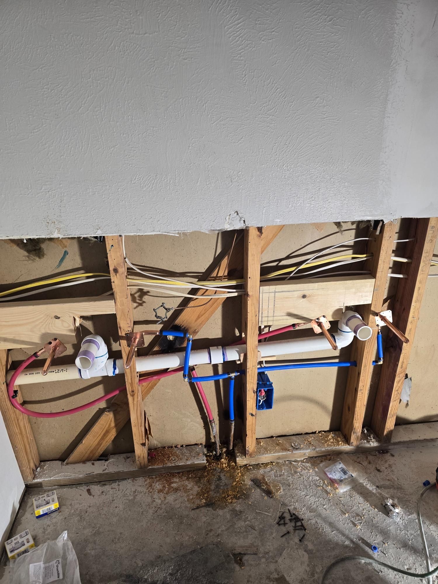Pipes and plumbing fixtures exposed inside a wall. PEX pipes are blue and white. Copper and white PVC fixtures connect pipes.