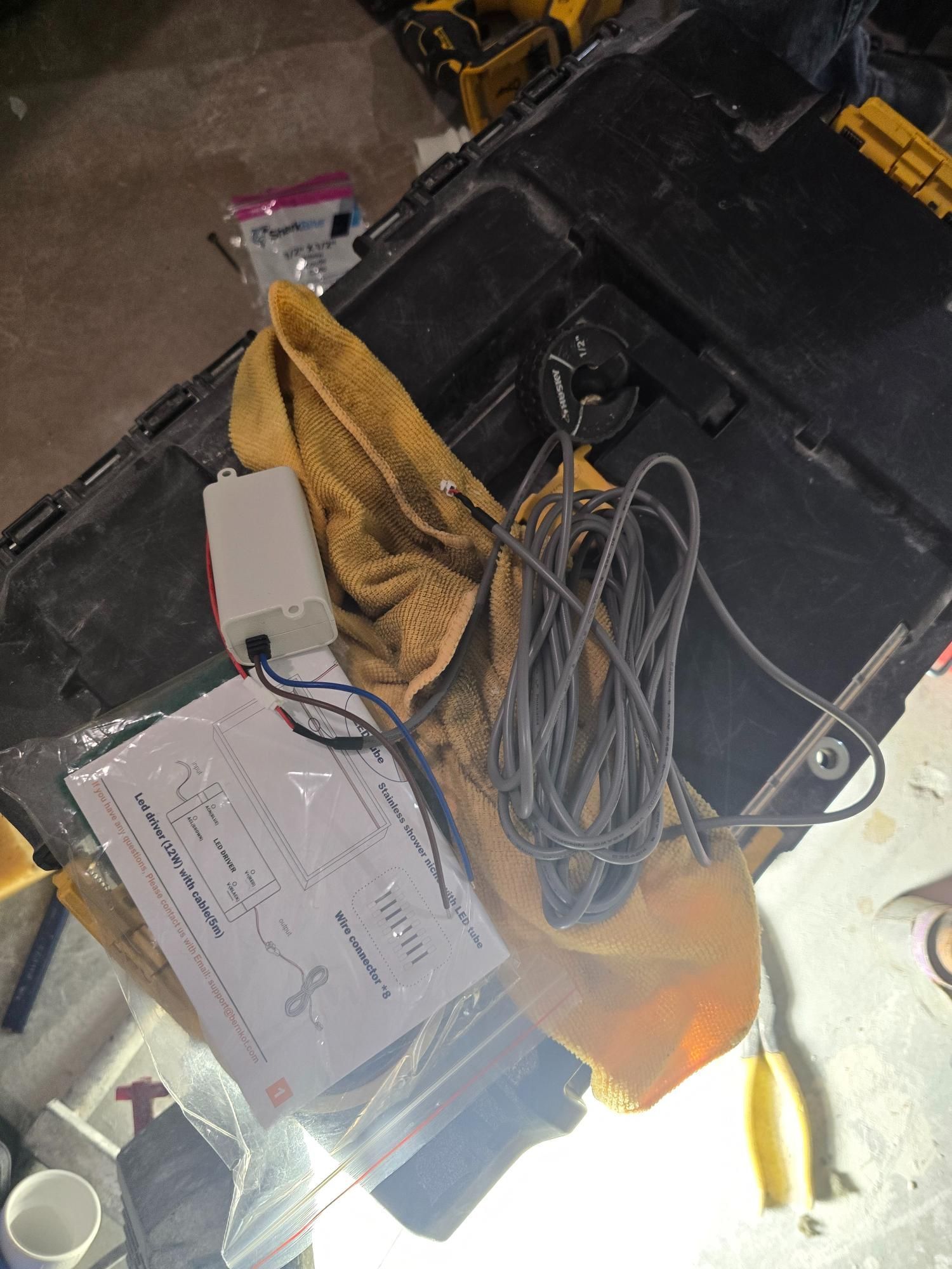 White electrical component, documentation, and coiled black wire on a toolbox with a yellow towel.