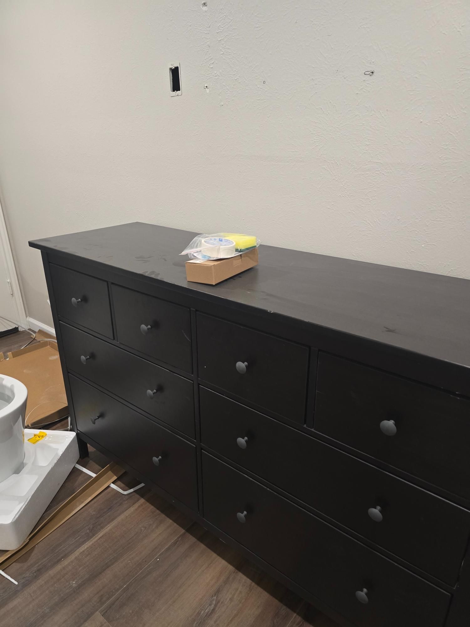 Black dresser with nine drawers against a beige wall, a small box sits on top.