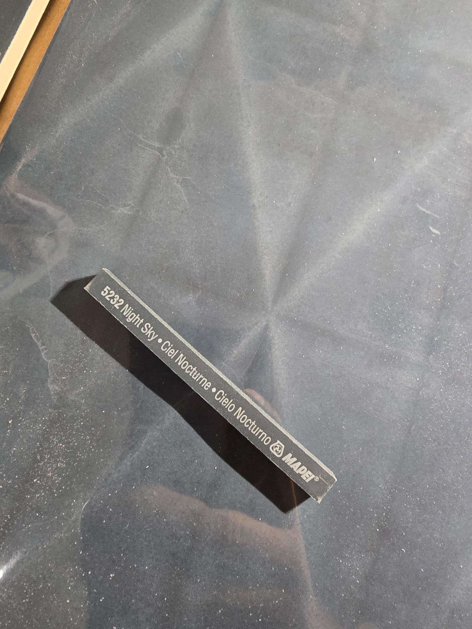 Small, dark grey tile sample with white text on a reflective surface.