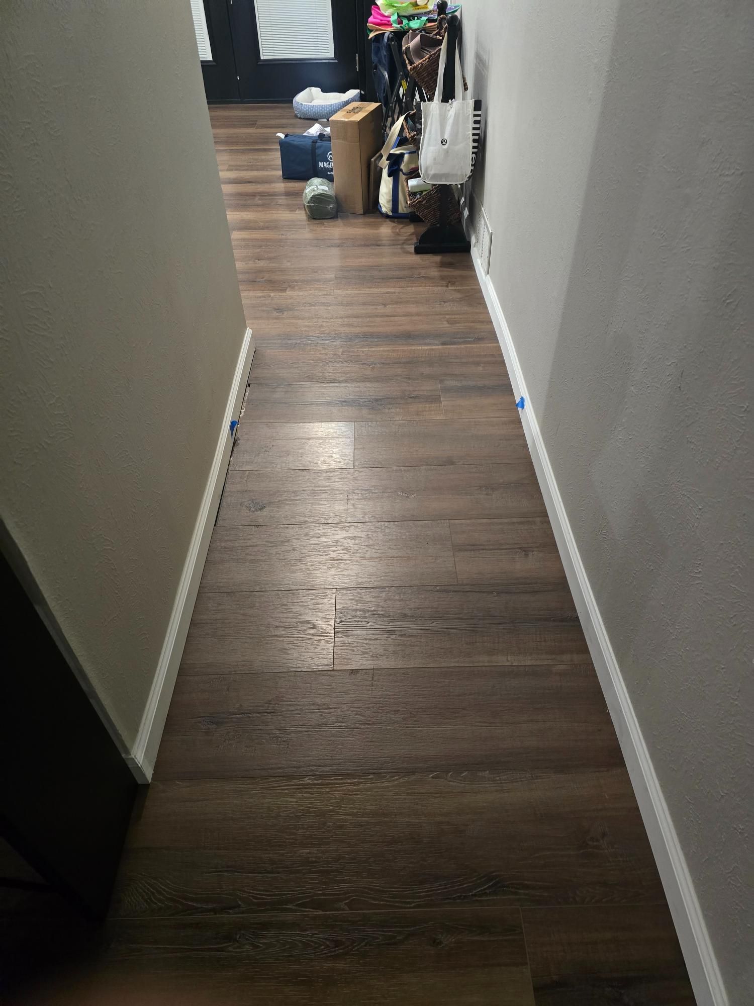 Narrow hallway with dark brown wood-look flooring, white trim, and gray walls. Some clutter at the far end.