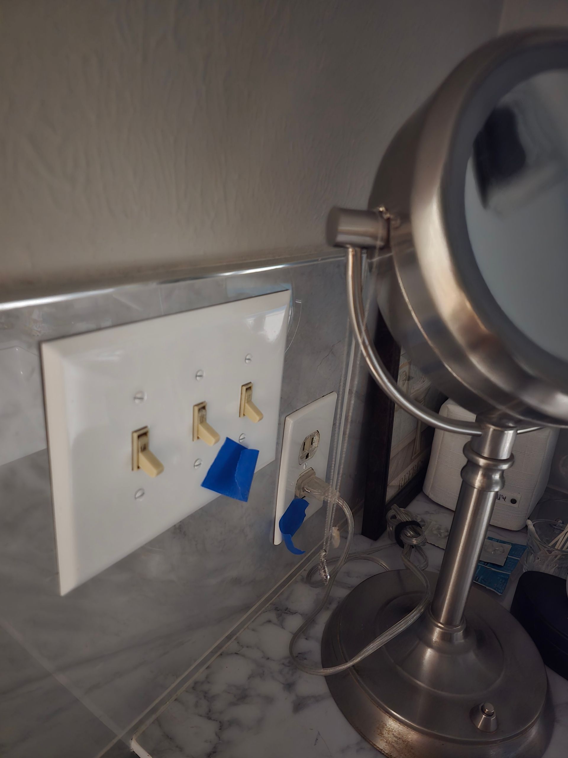 Bathroom with a mirror, light switches, and an outlet; blue tape on outlet and switches.