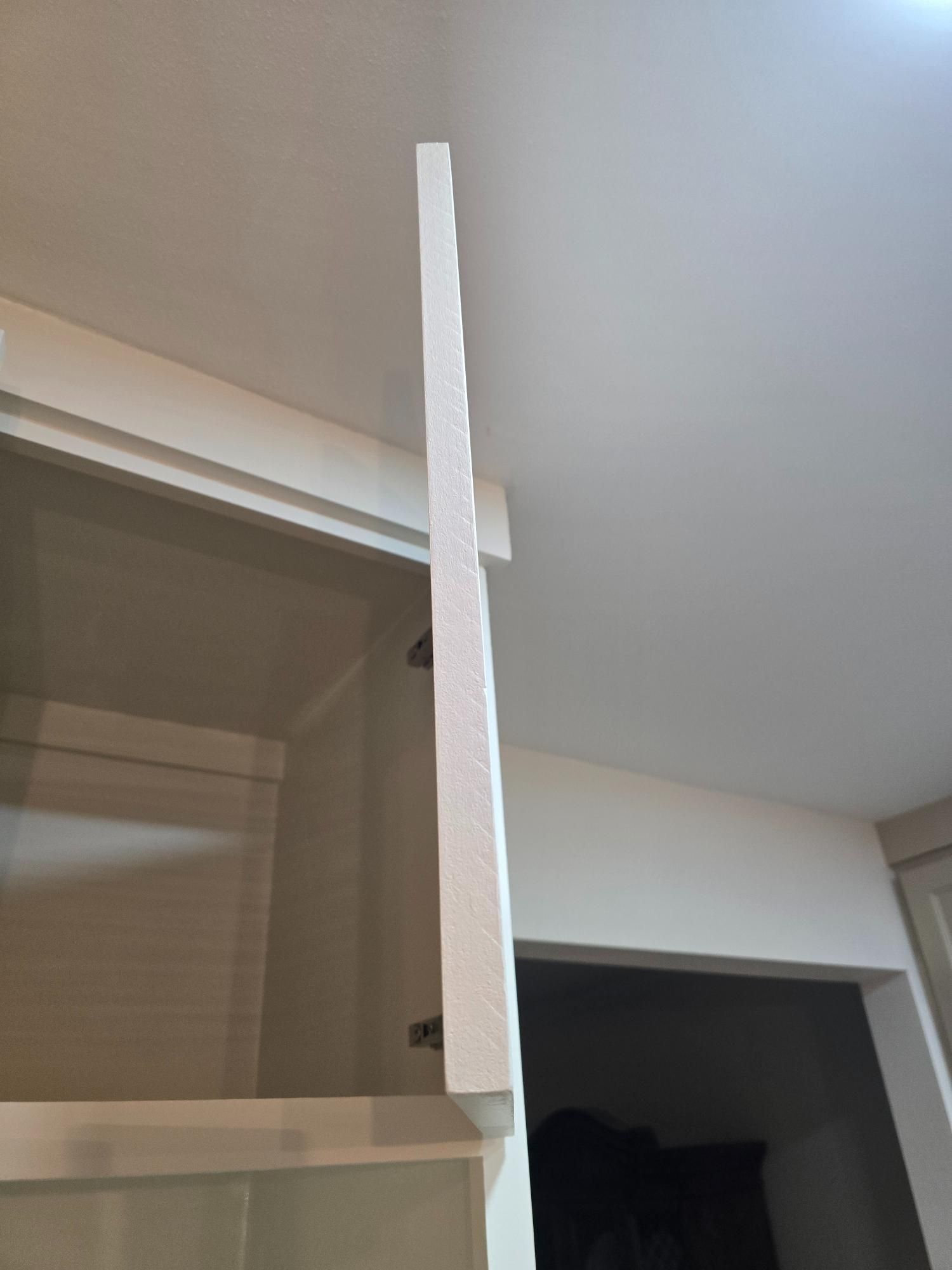 Open white kitchen cabinet, with white trim against a white ceiling.