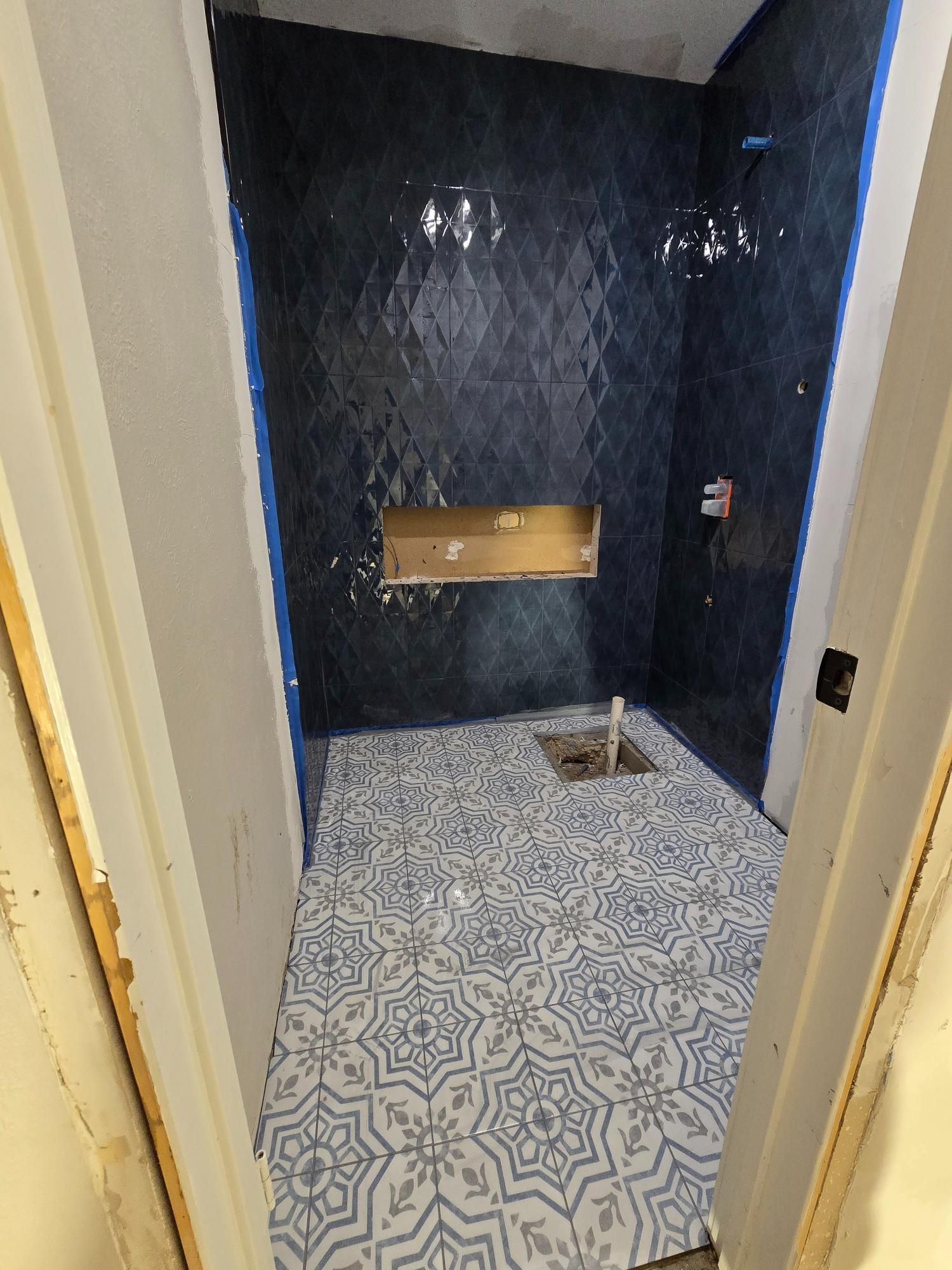 Bathroom under construction with dark blue wall tiles and patterned floor tiles.