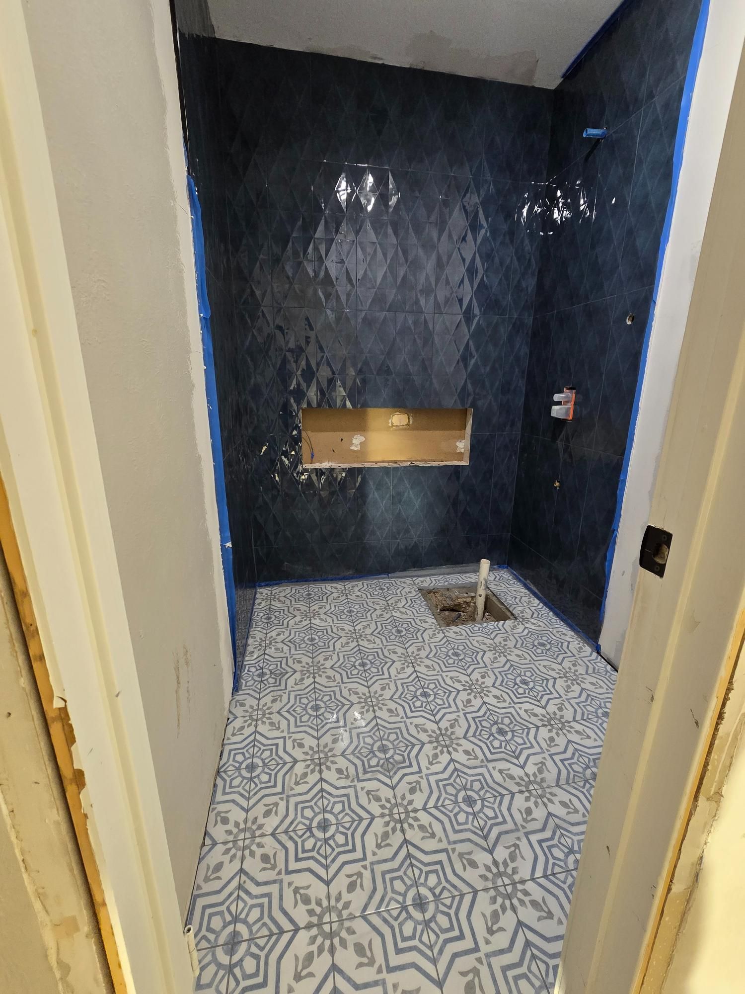 Bathroom under construction: blue tiled shower and patterned floor with an open shower niche.