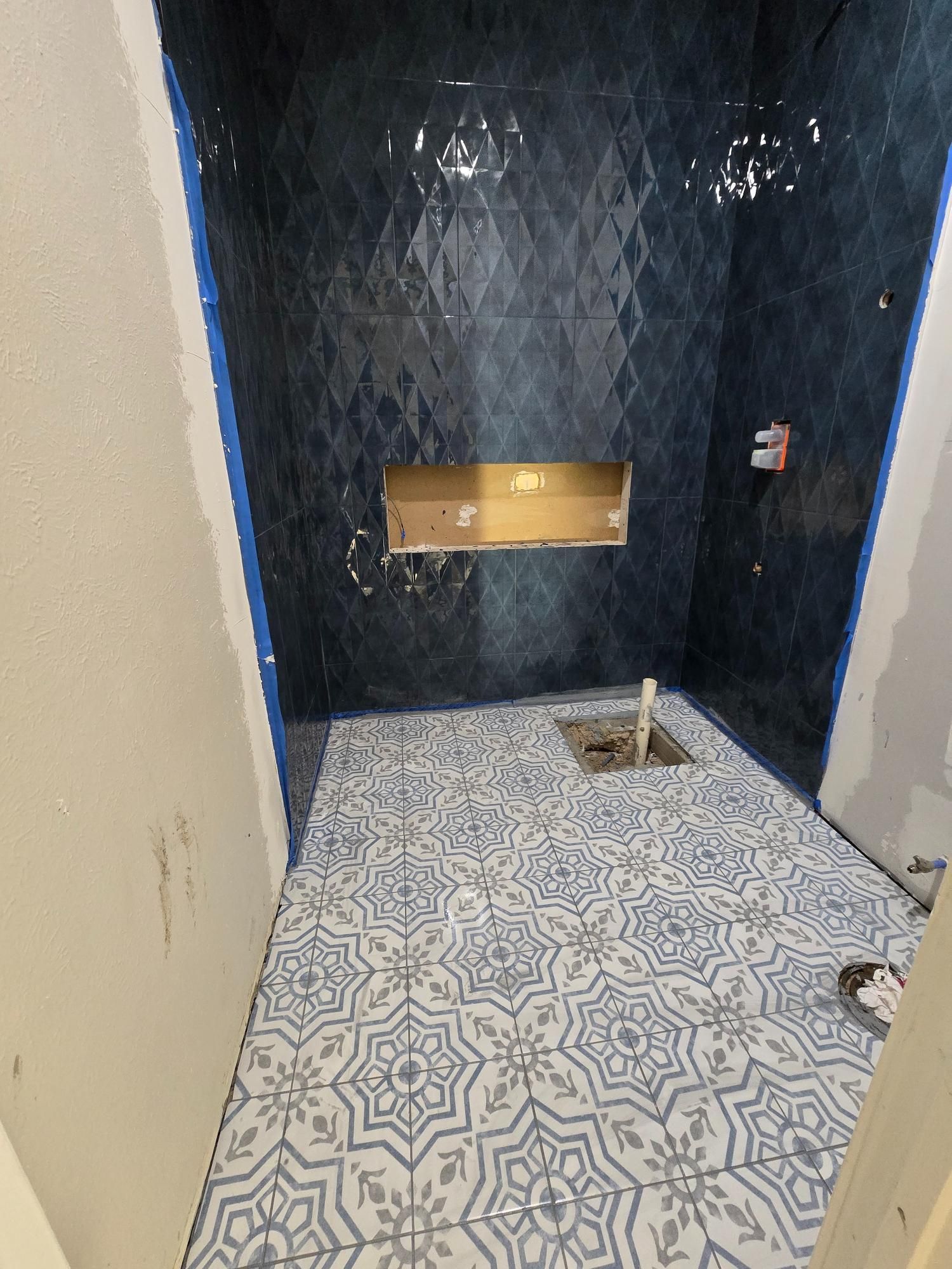 Bathroom under construction with blue patterned tiles and shower niche.