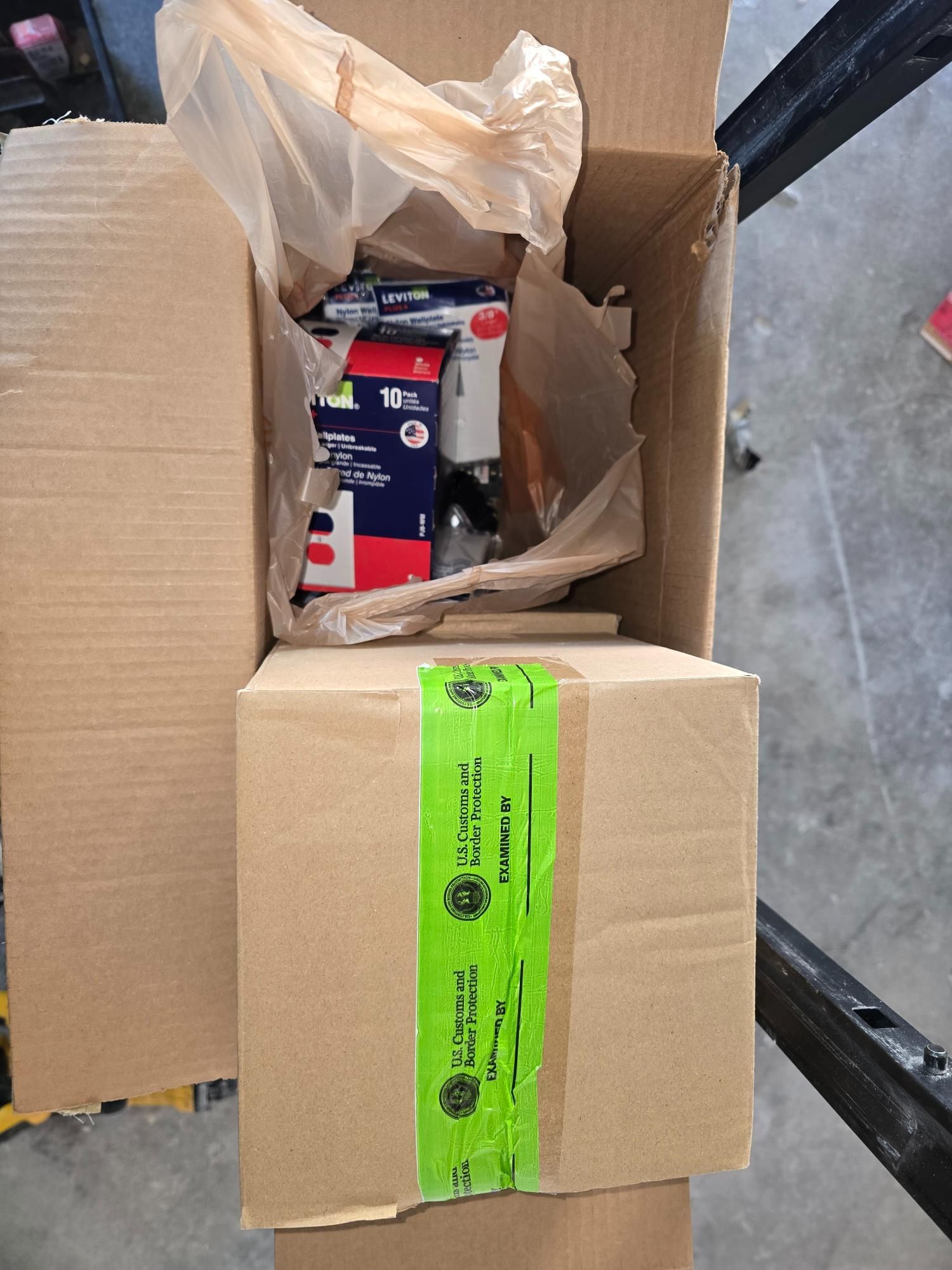 Cardboard box partially open with green tape; contents include supplies in a plastic bag.