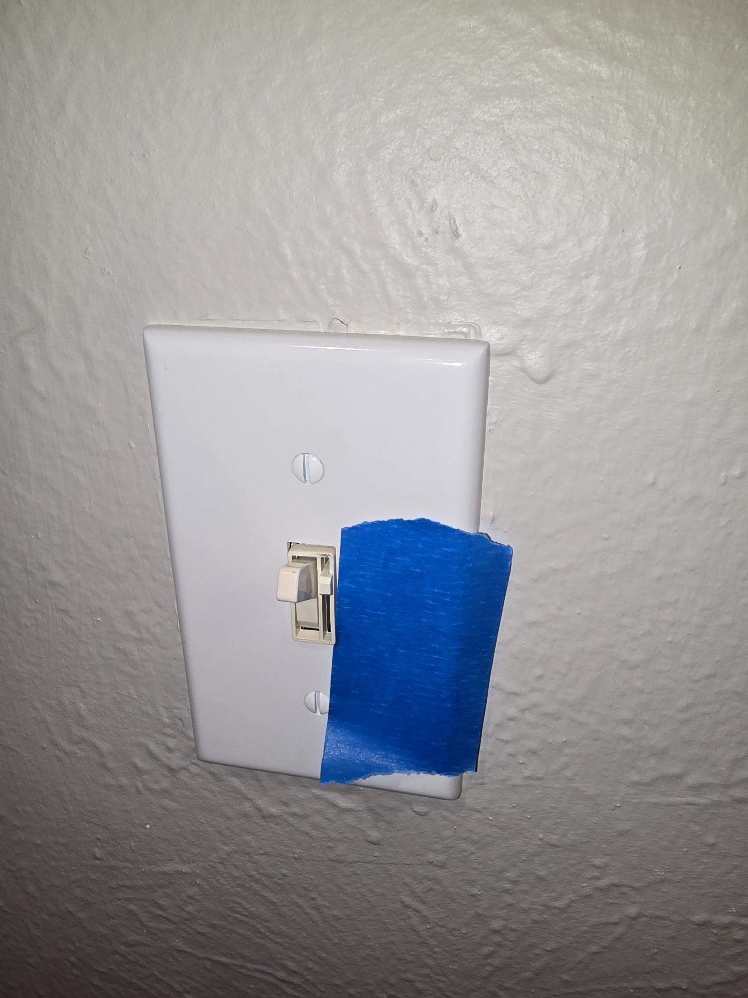 White light switch plate on a textured, off-white wall; blue tape covers part of the switch.