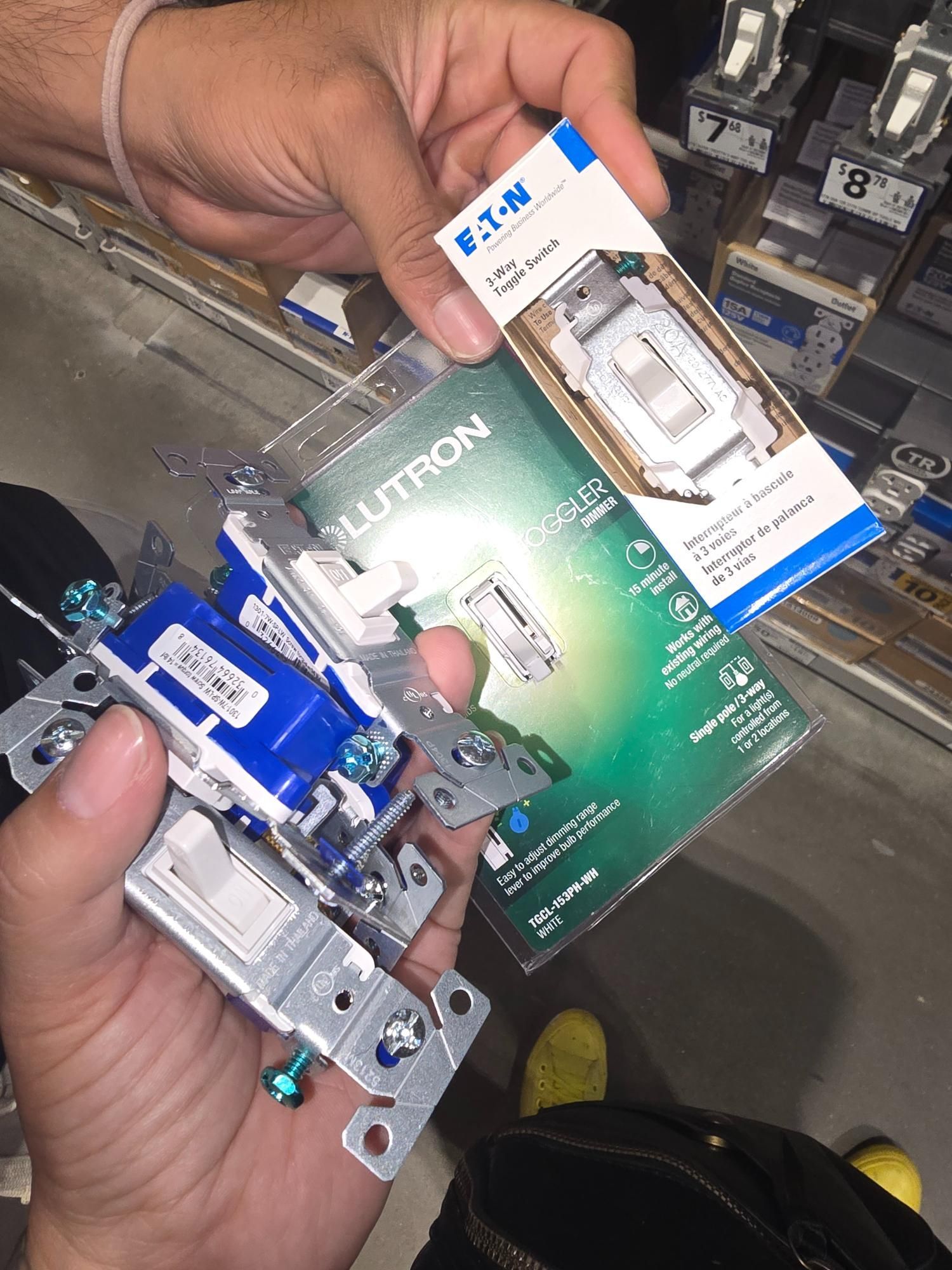 Hands holding light switches and packaging in a store. Blue, white, and silver colors are visible.
