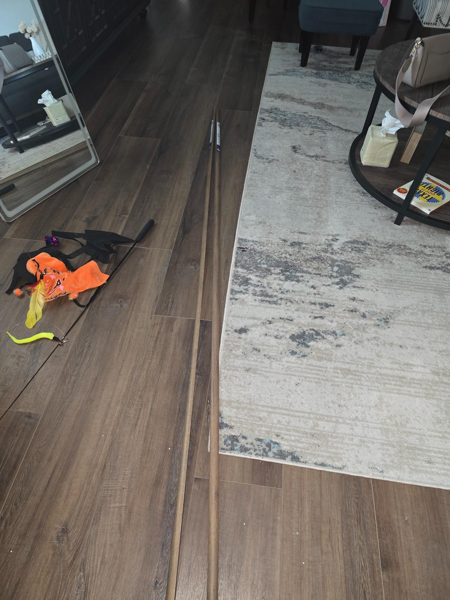 Wooden bow and arrow on wood floor, with cat toy and rug visible.