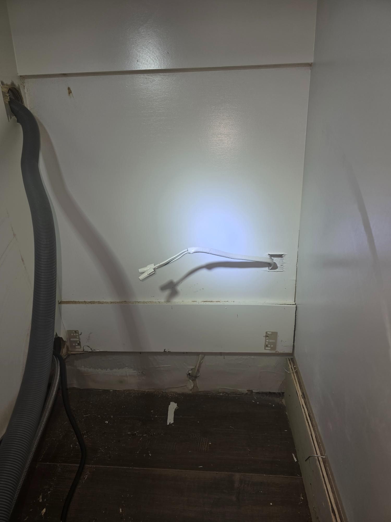 White wall with exposed electrical wires and a flexible gray tube.
