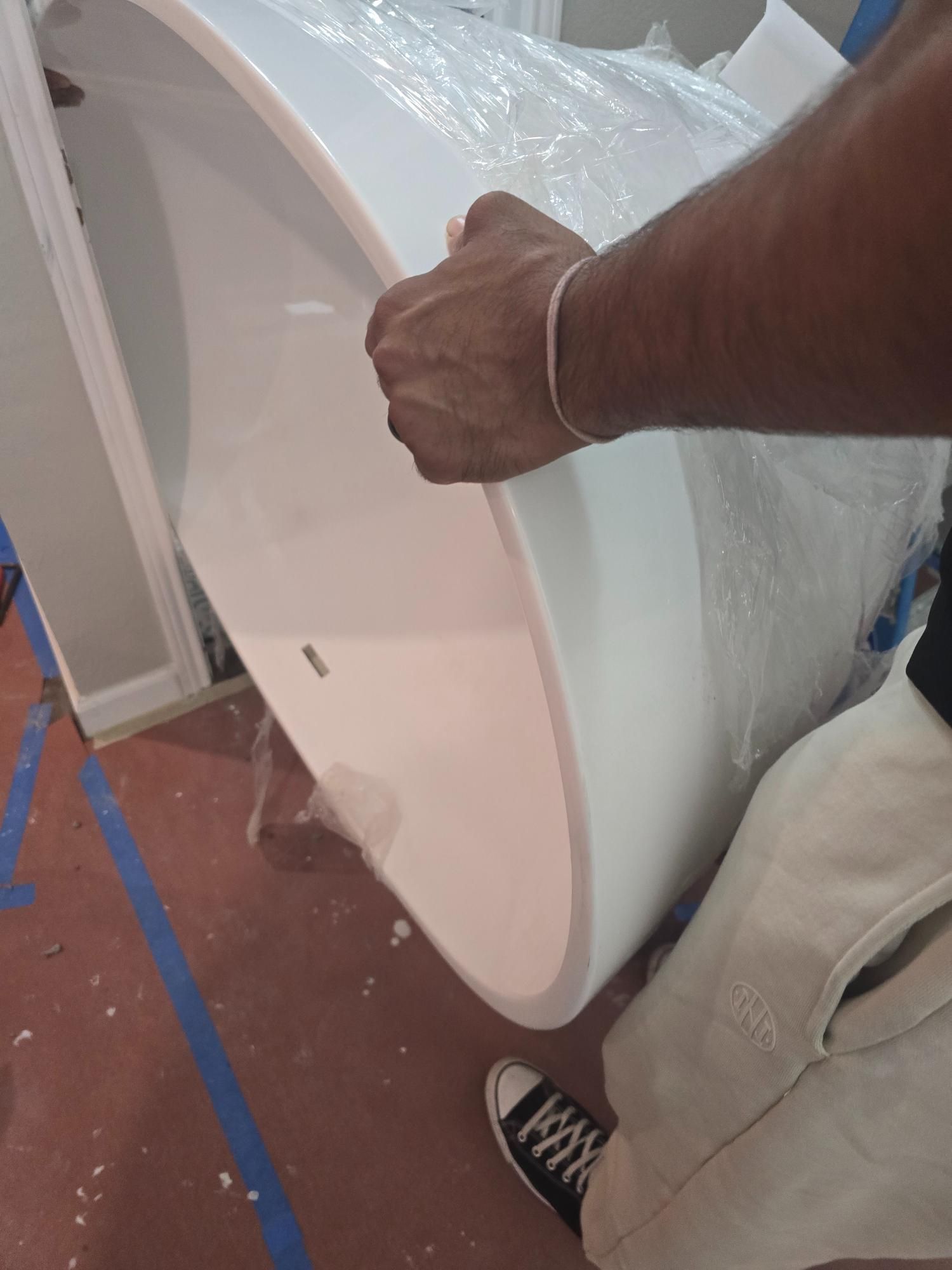 Person holding a white bathtub wrapped in plastic, indoors, with a red floor.