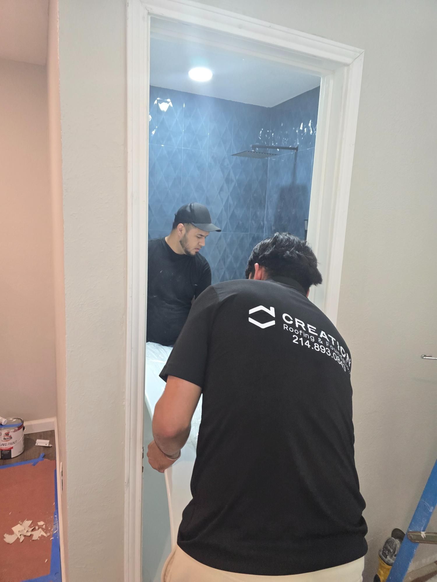 Two workers installing a shower door. One worker is inside the shower. The other worker is outside the shower.