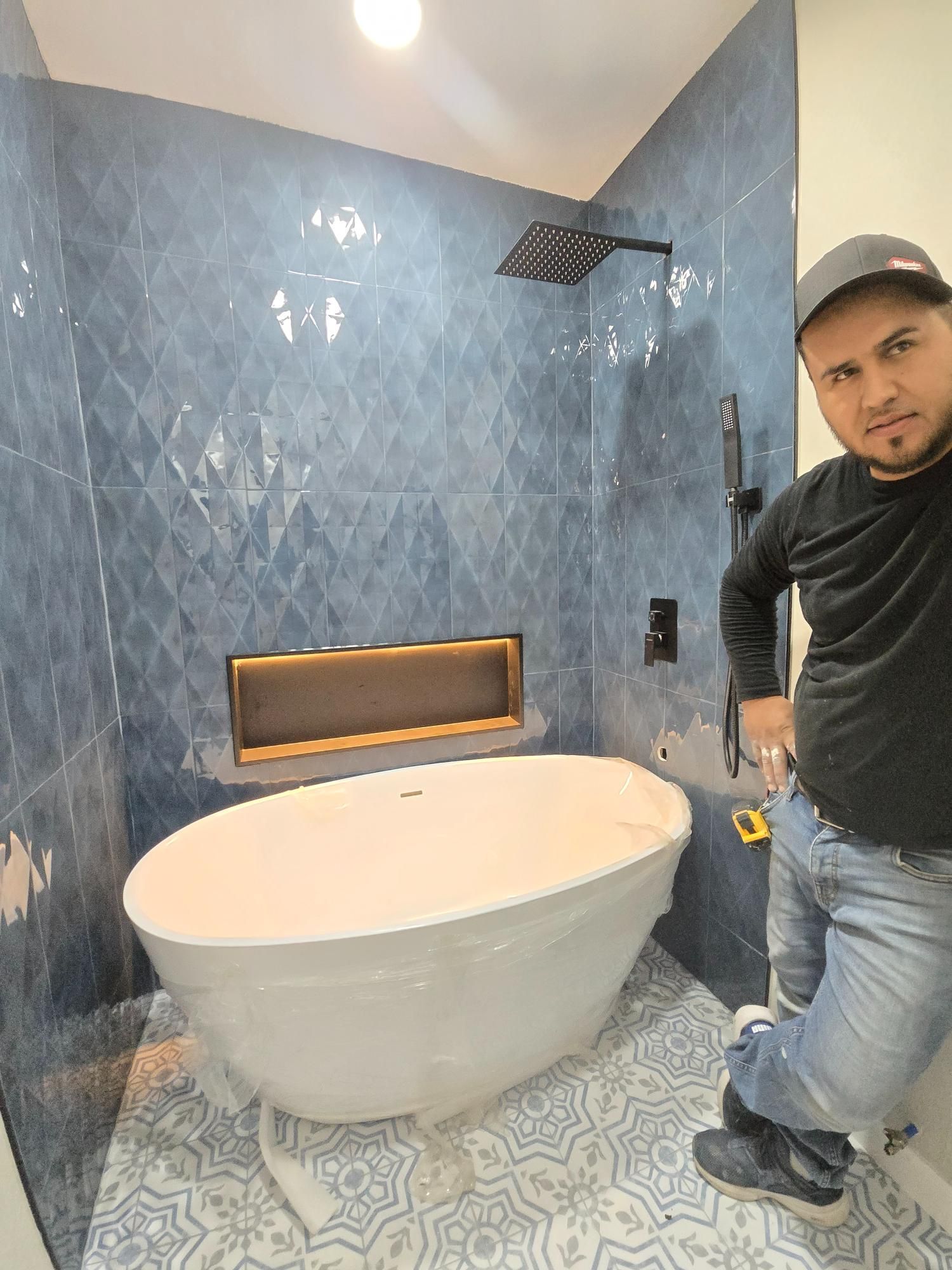 Man standing in a newly tiled bathroom with a tub and shower.