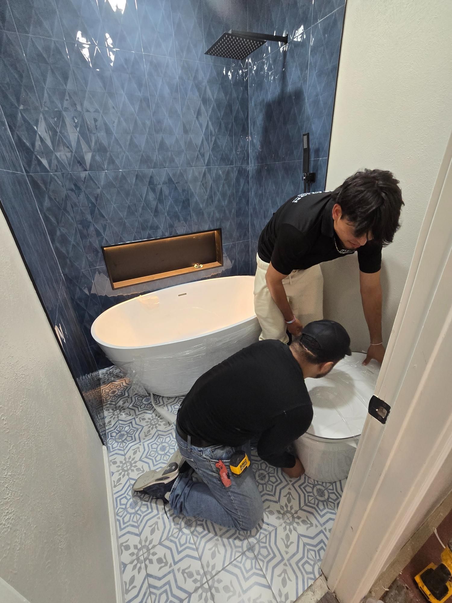 Two people installing tile in a blue and white tiled bathroom with a white tub.