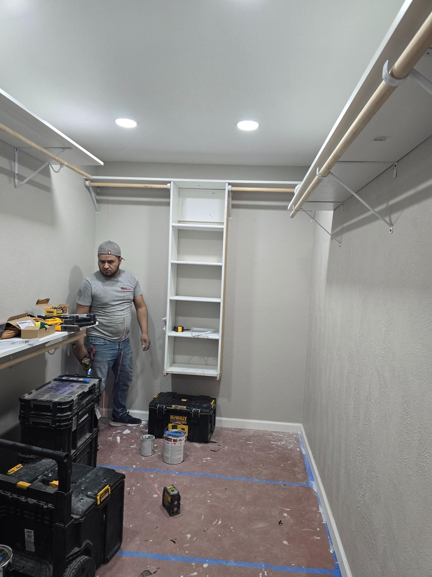 Person in a closet with tools, installing shelves. White shelves, grey walls, red floor.