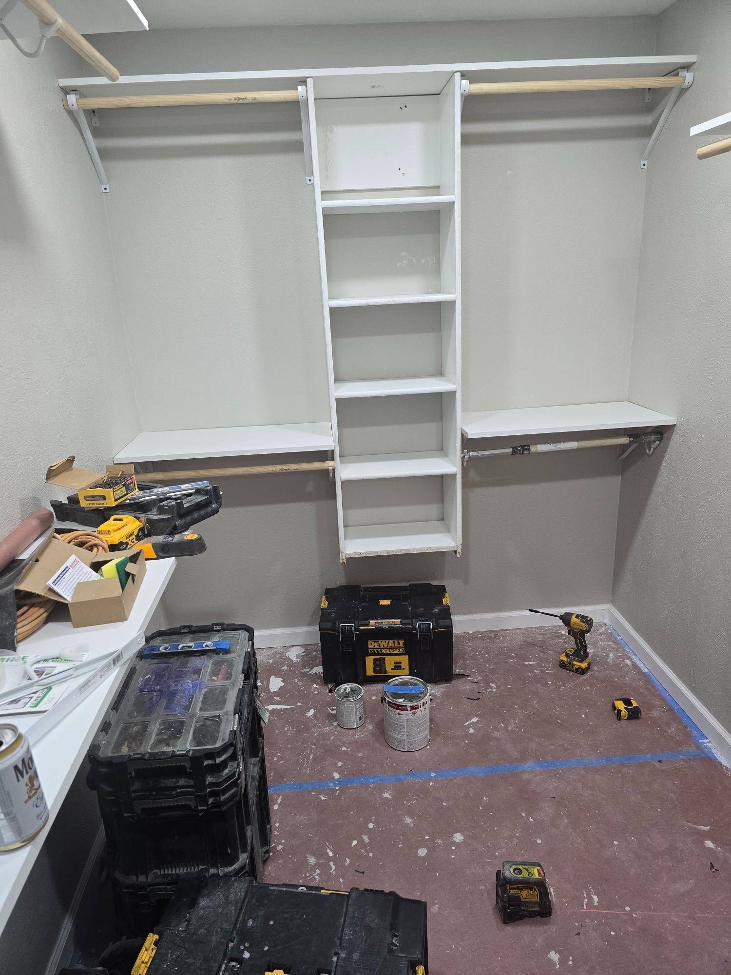 A closet with white shelves and rods under construction, with tools and materials scattered on the floor.