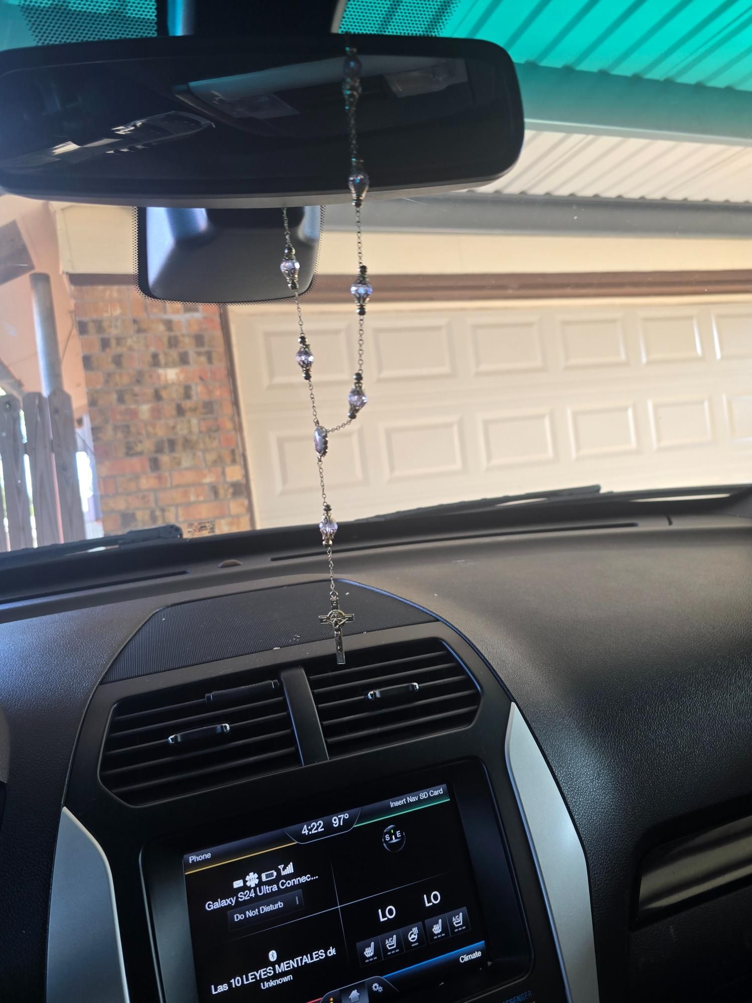 Rosary hanging from a car's rearview mirror, interior view, dashboard and garage door in background.