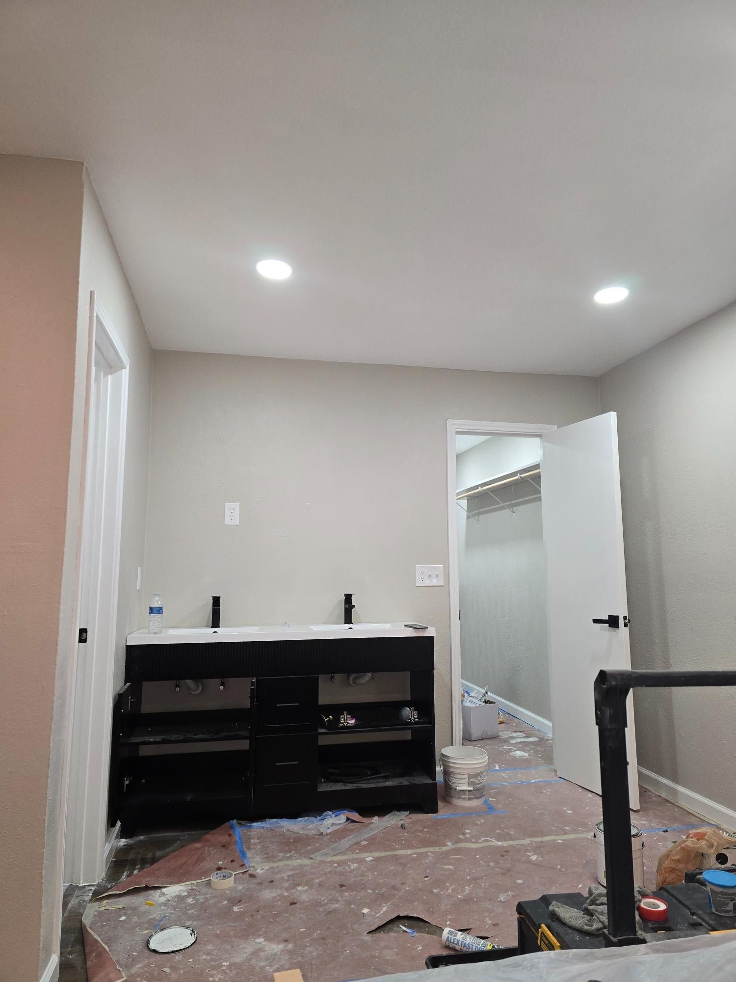Bathroom under construction; black vanity, white walls, open door to closet, unfinished floor.