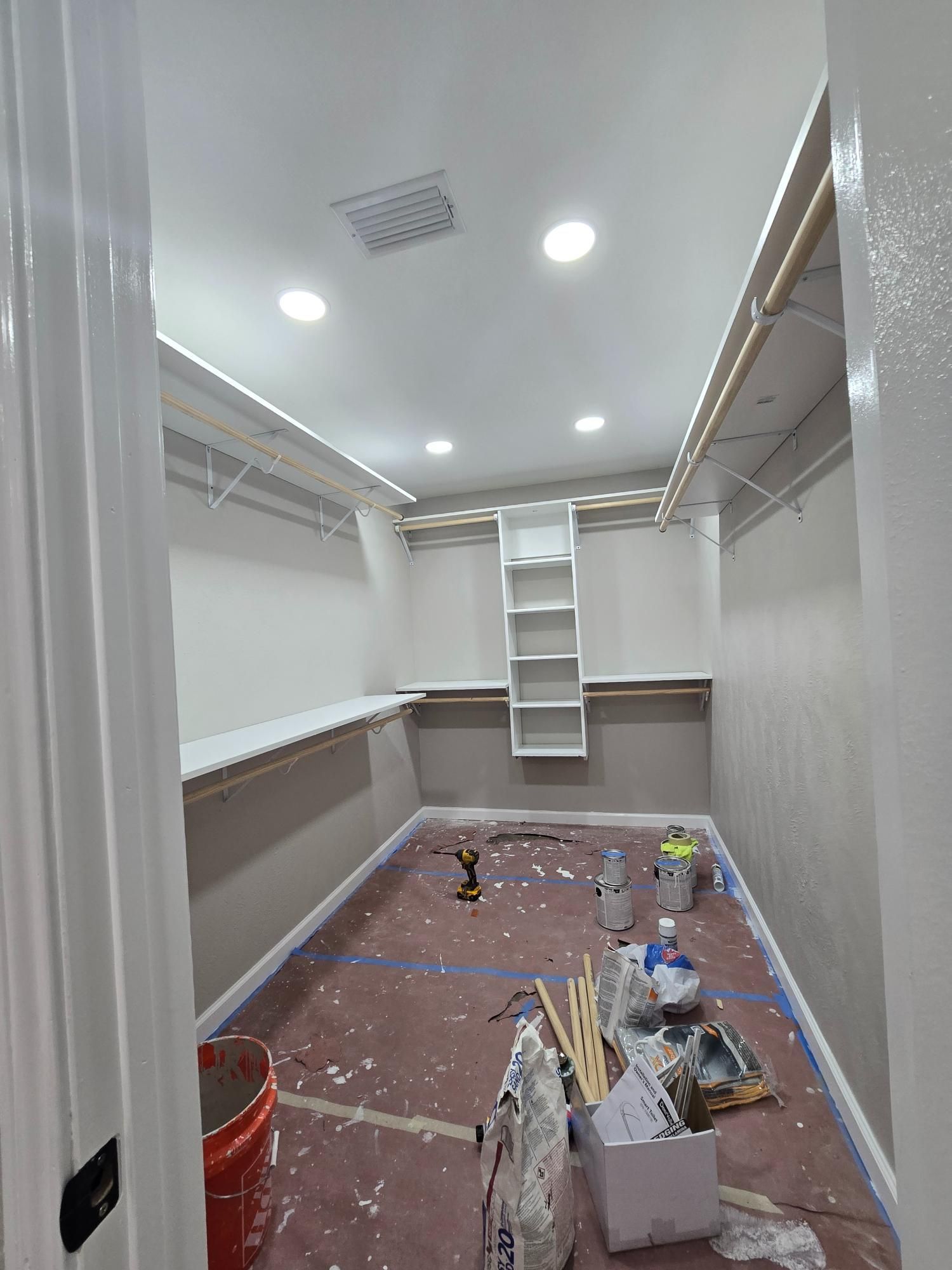 Empty closet with shelves, lights, and paint supplies on the floor; freshly painted white walls and trim.