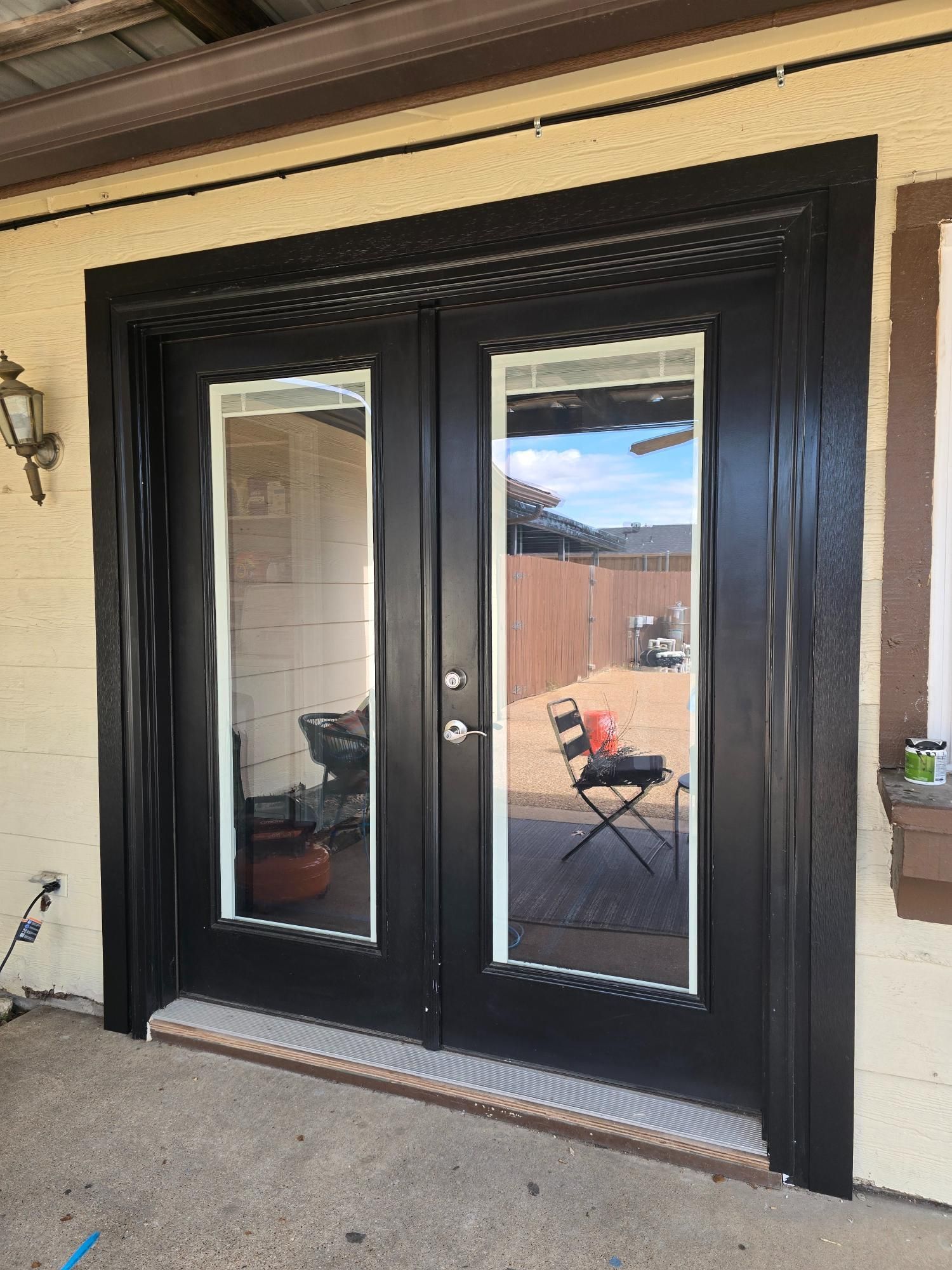 Black double doors with glass panels and white trim, set in a light-colored wall with a concrete slab.