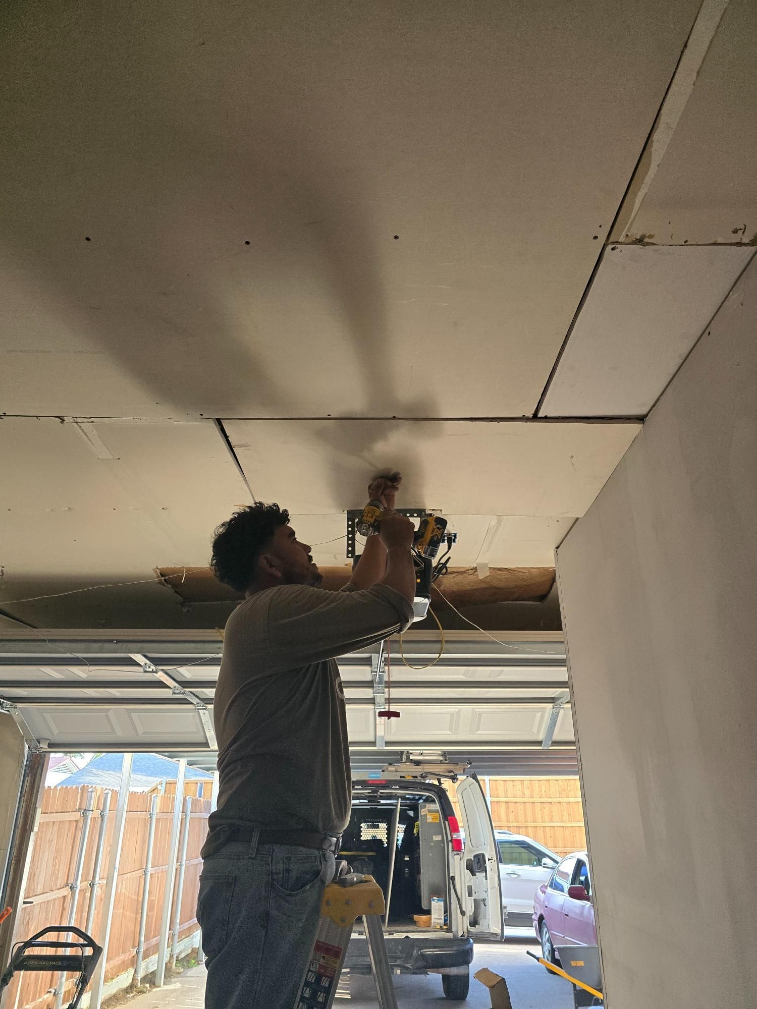 Man cutting drywall on a ceiling with a circular saw in a garage.