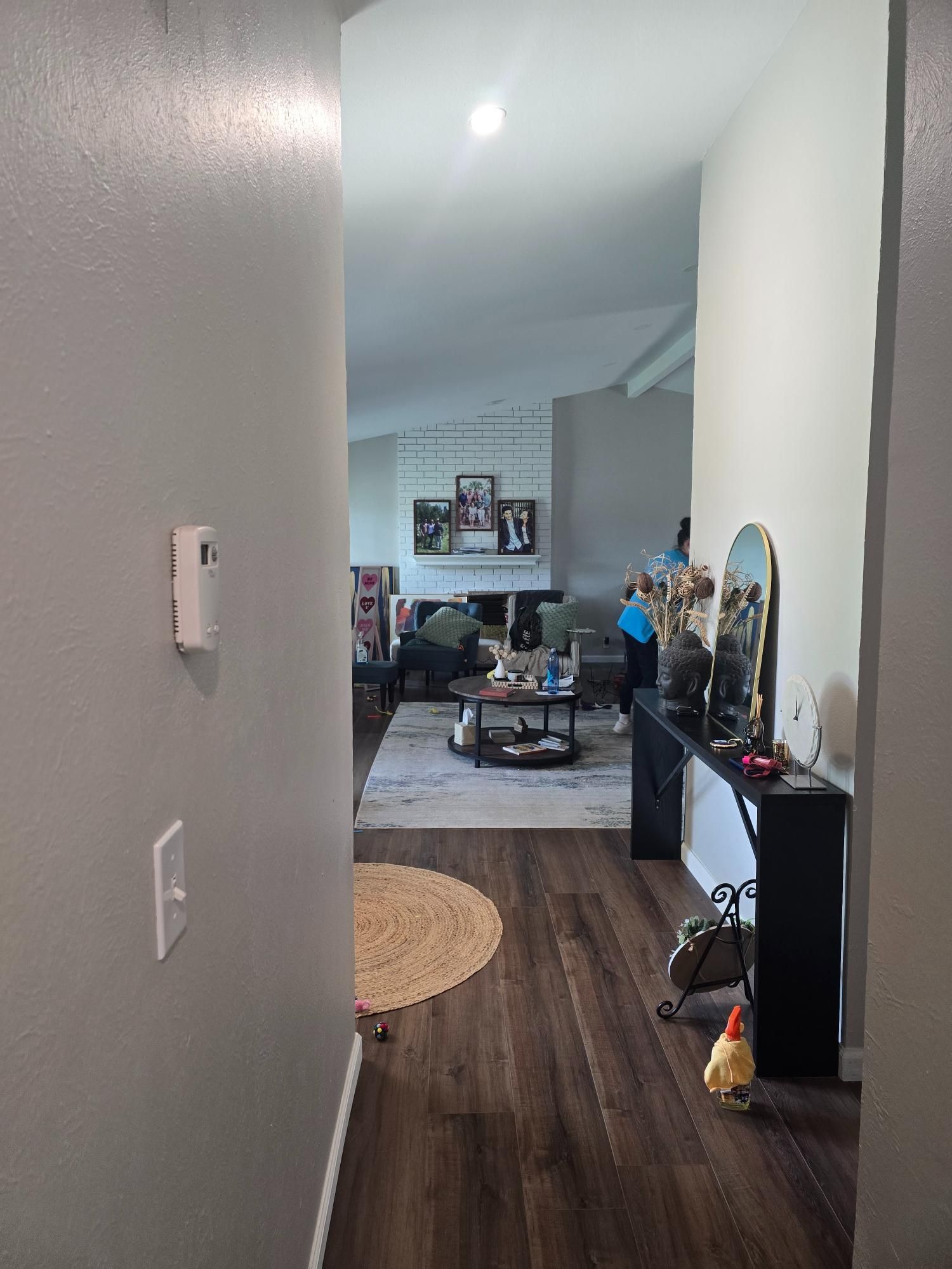 Entryway with dark wood-look floor leading to living room. White walls, a black console table, and a rug are visible.