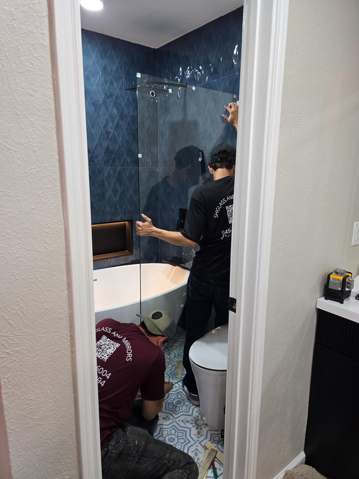 Two people installing a glass shower door in a bathroom. One stands, the other kneels.
