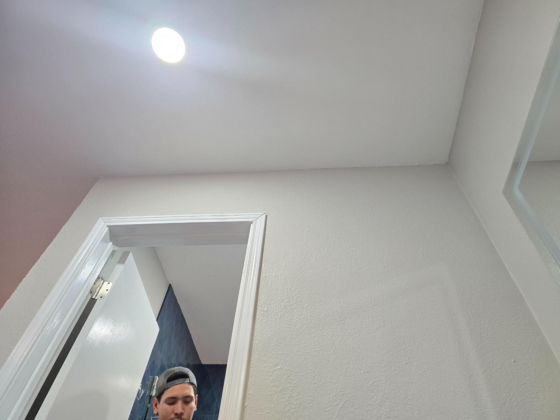 Man in doorway of a bathroom, looking at the camera. White door frame, walls, and ceiling.