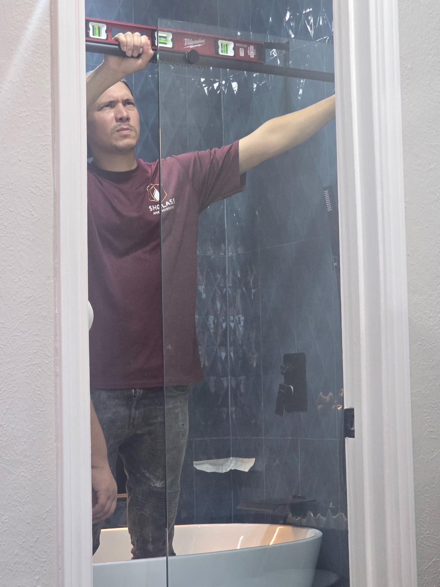 Man holding a level, checking a frameless glass shower door in a bathroom.