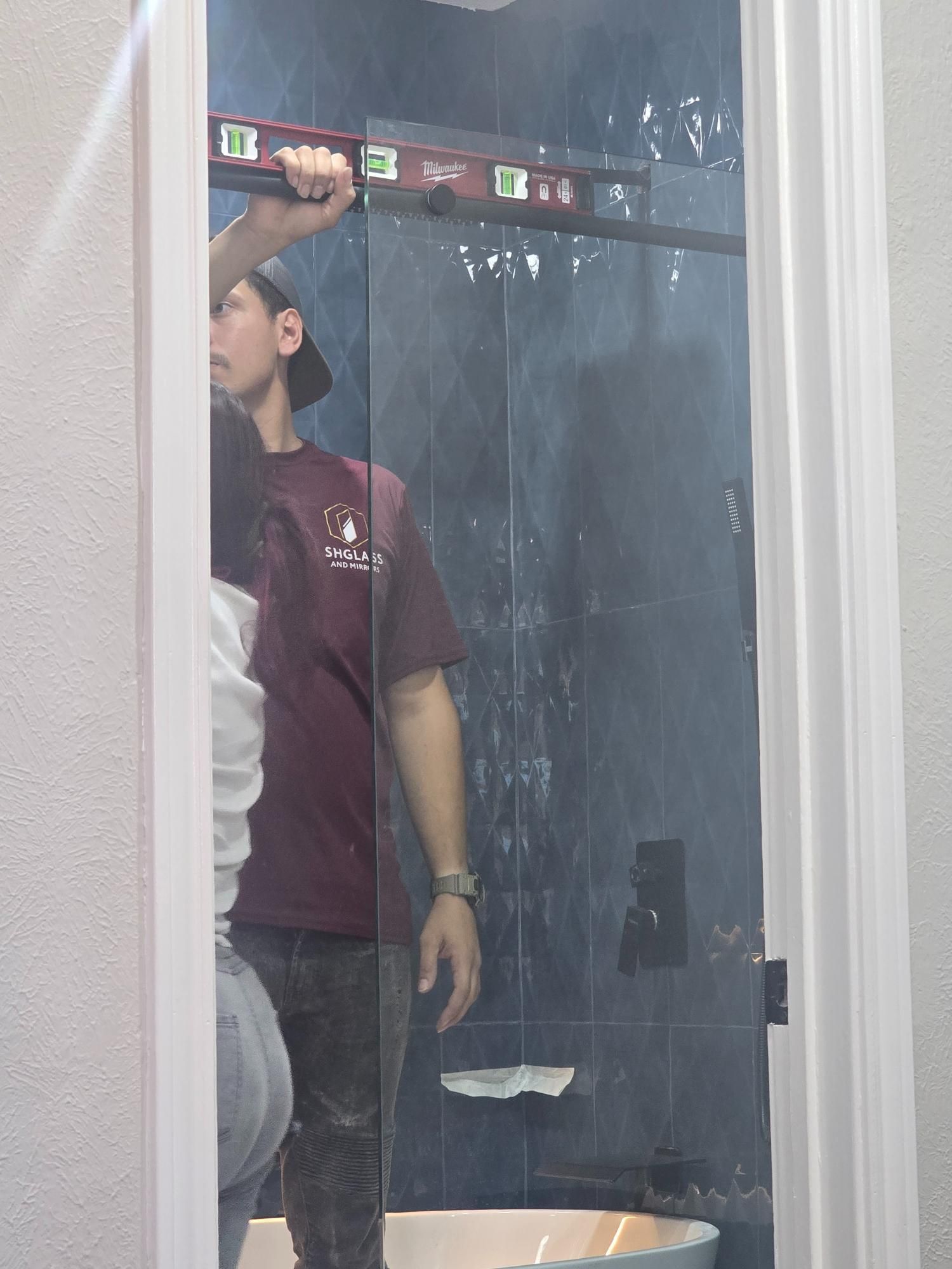 Man using a level to install a shower door in a bathroom.