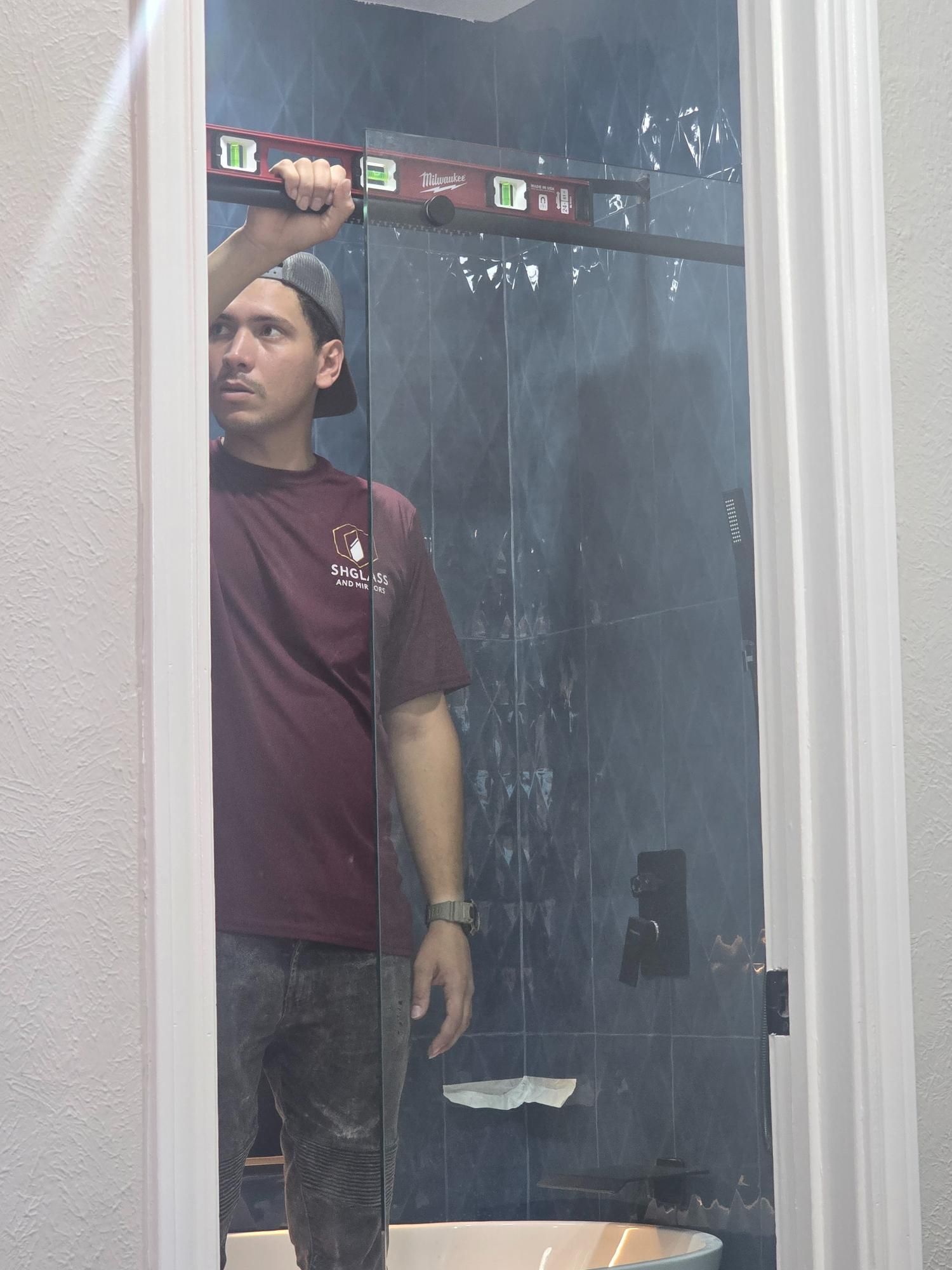Man using level, checking a shower door, inside a bathroom.