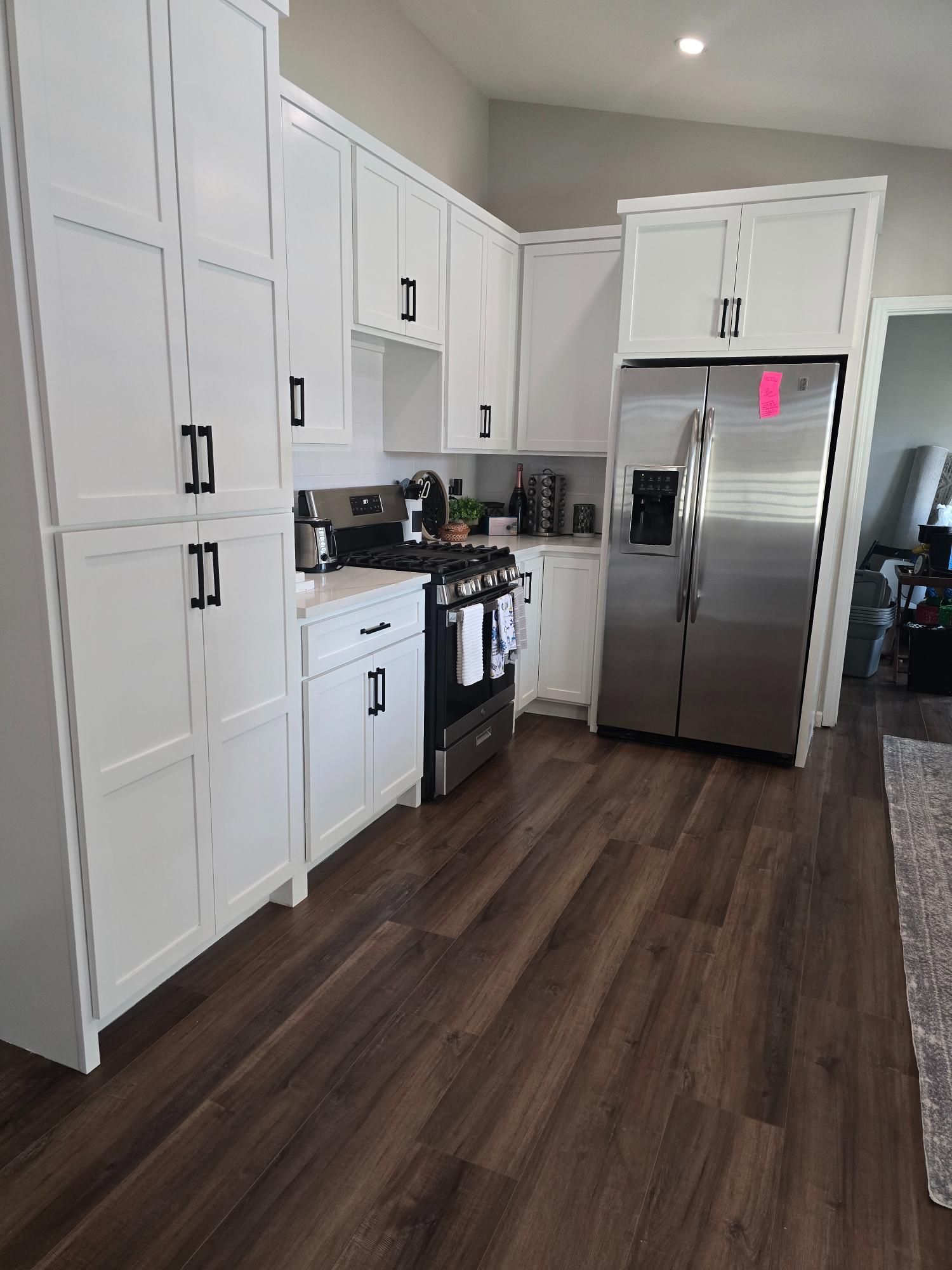 White kitchen cabinets with black hardware, stainless steel fridge, and dark wood floors.