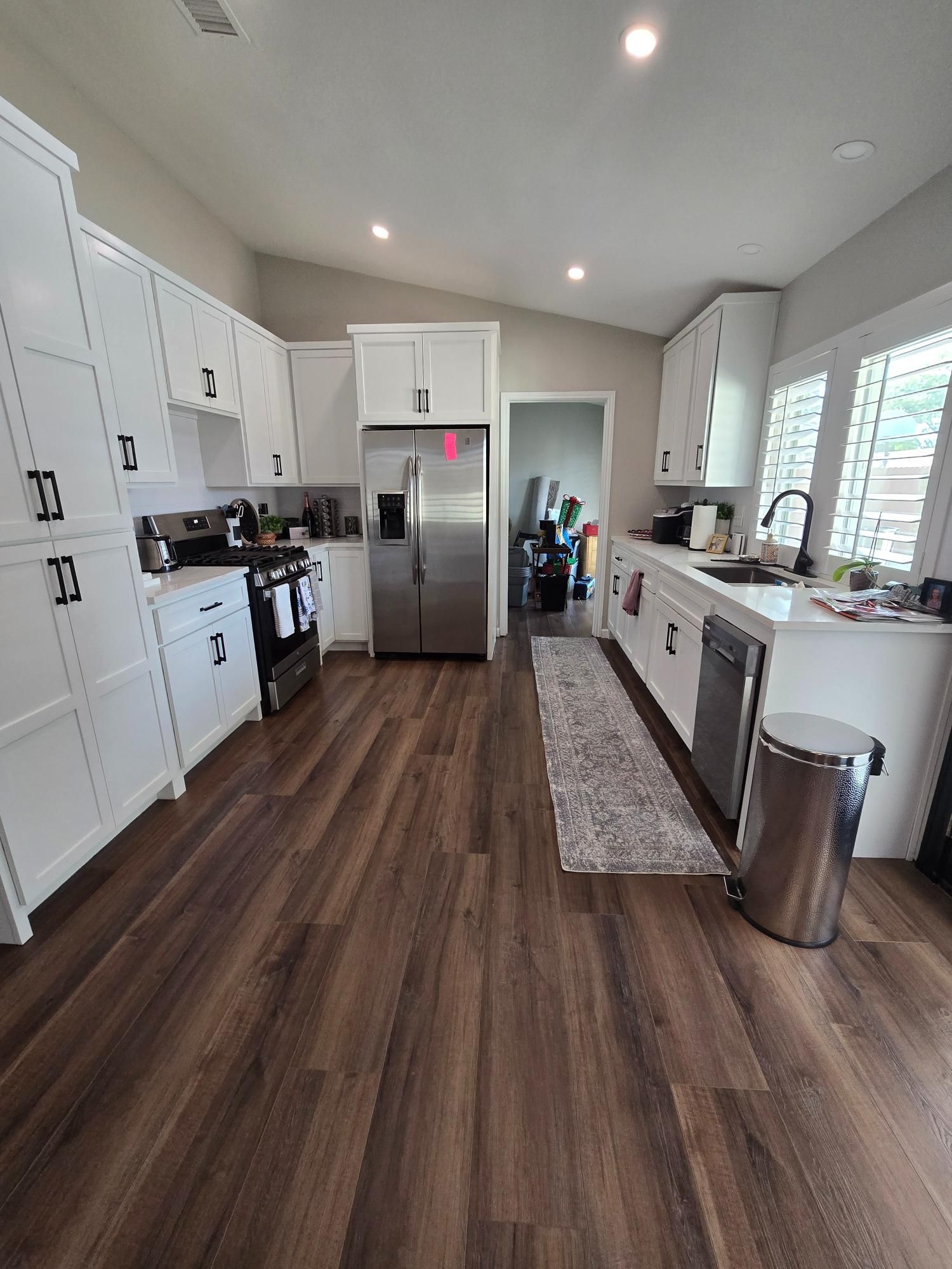 White kitchen with stainless steel appliances, dark wood flooring, and overhead cabinets.