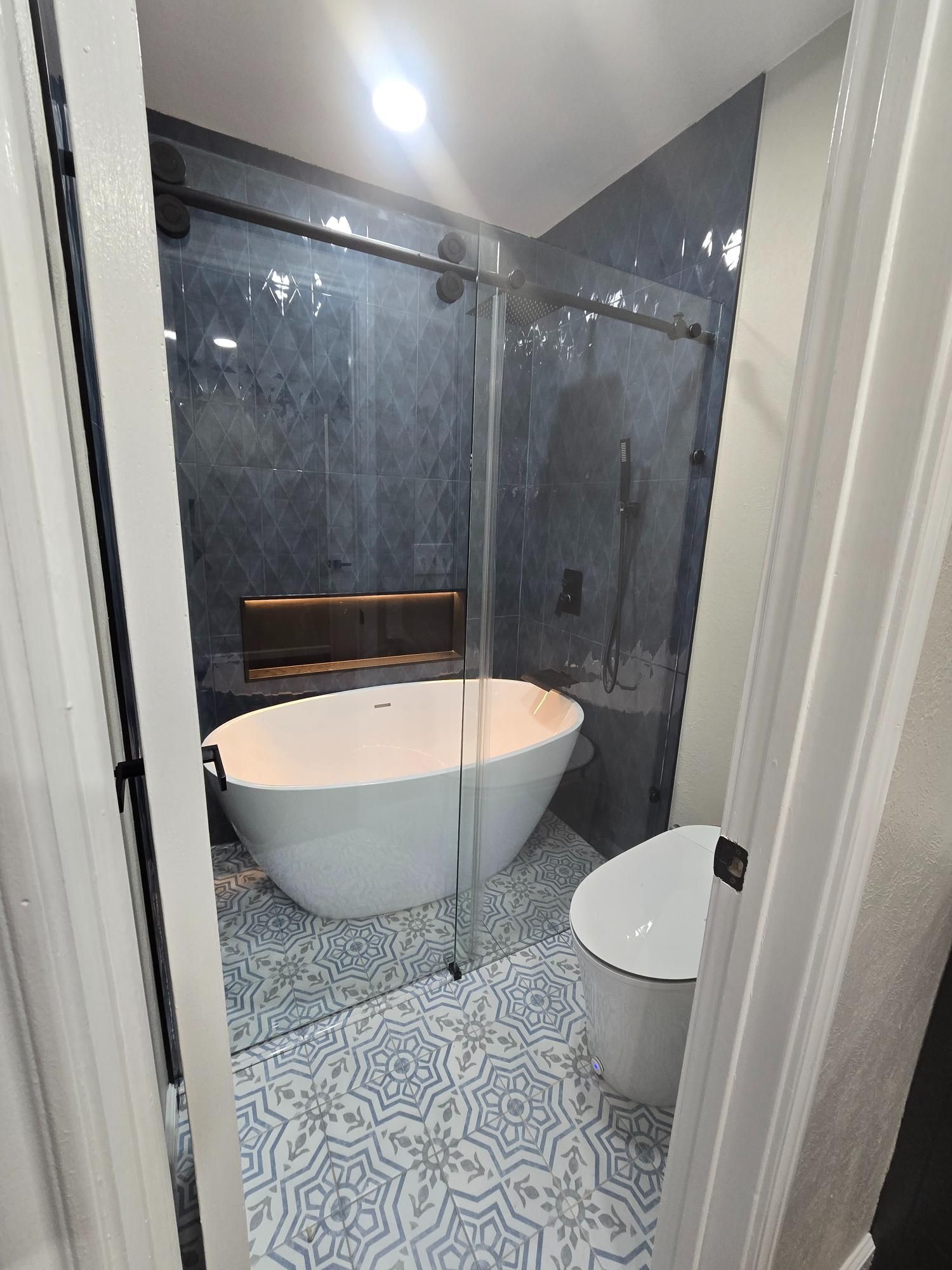 Modern bathroom with a white bathtub and glass shower enclosure. Blue patterned tile flooring.