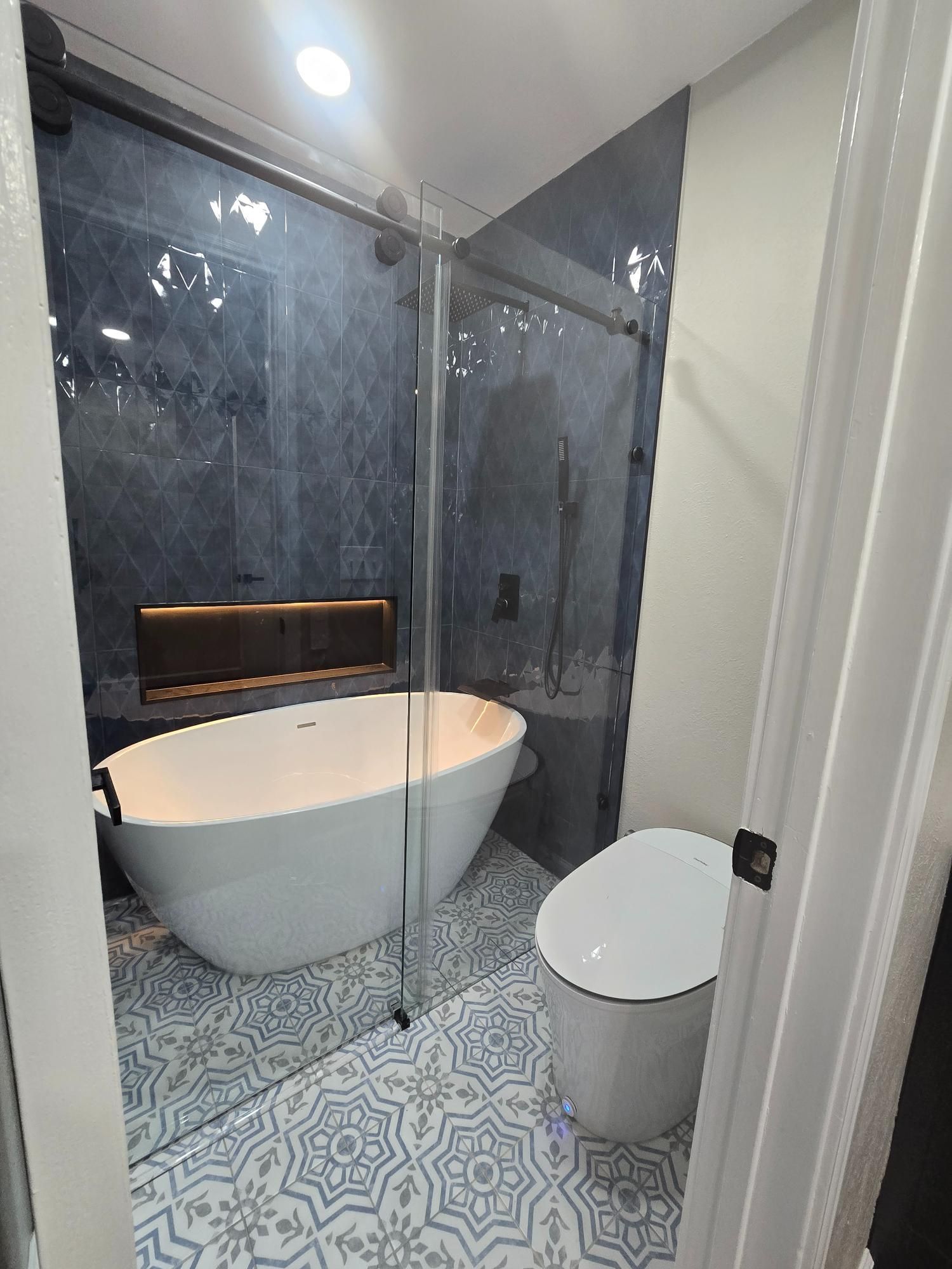 Bathroom with a white tub, blue and white patterned tile, and a glass shower enclosure.