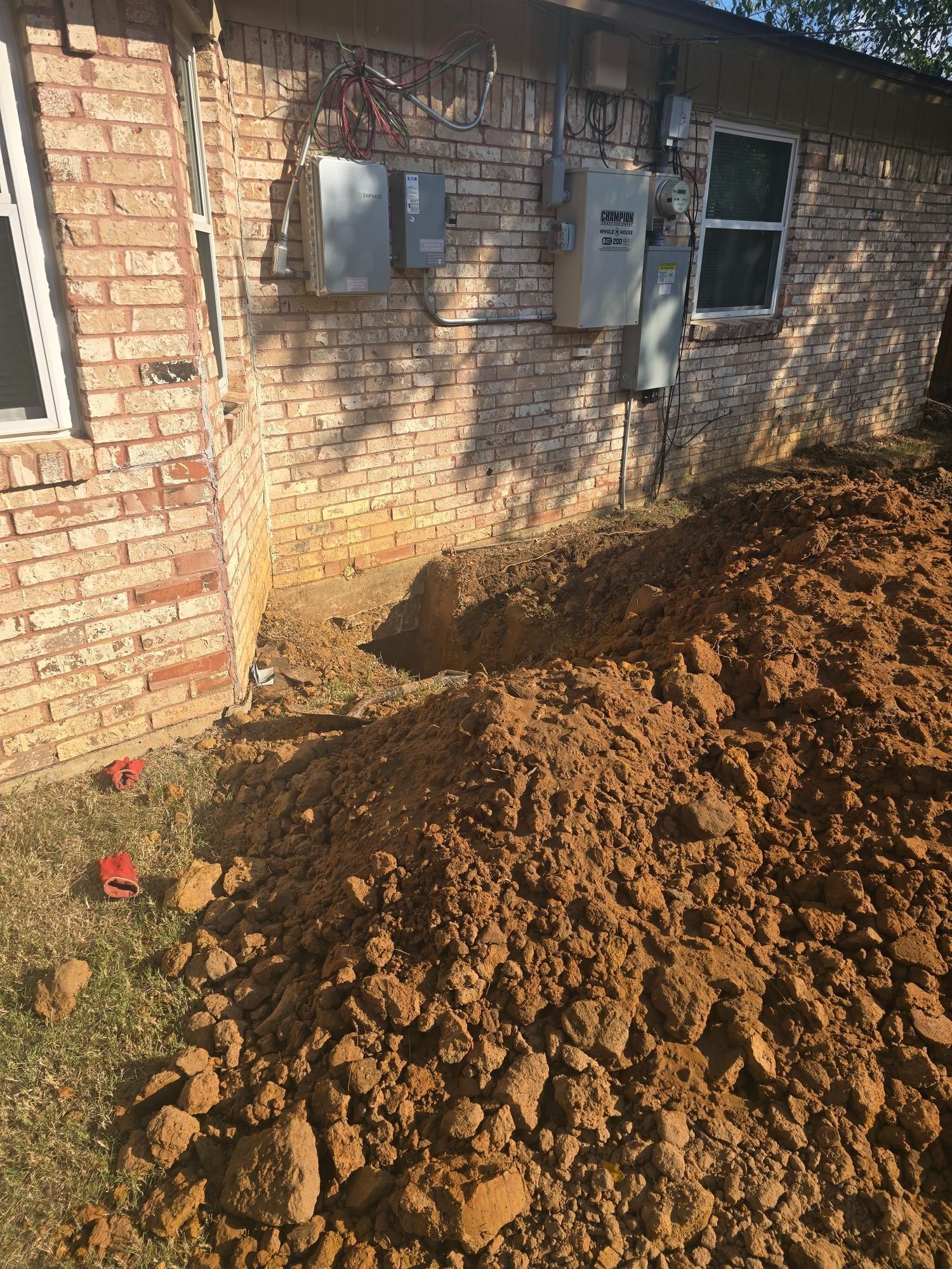 Pile of dirt next to a brick building; hole dug in the ground near the building.