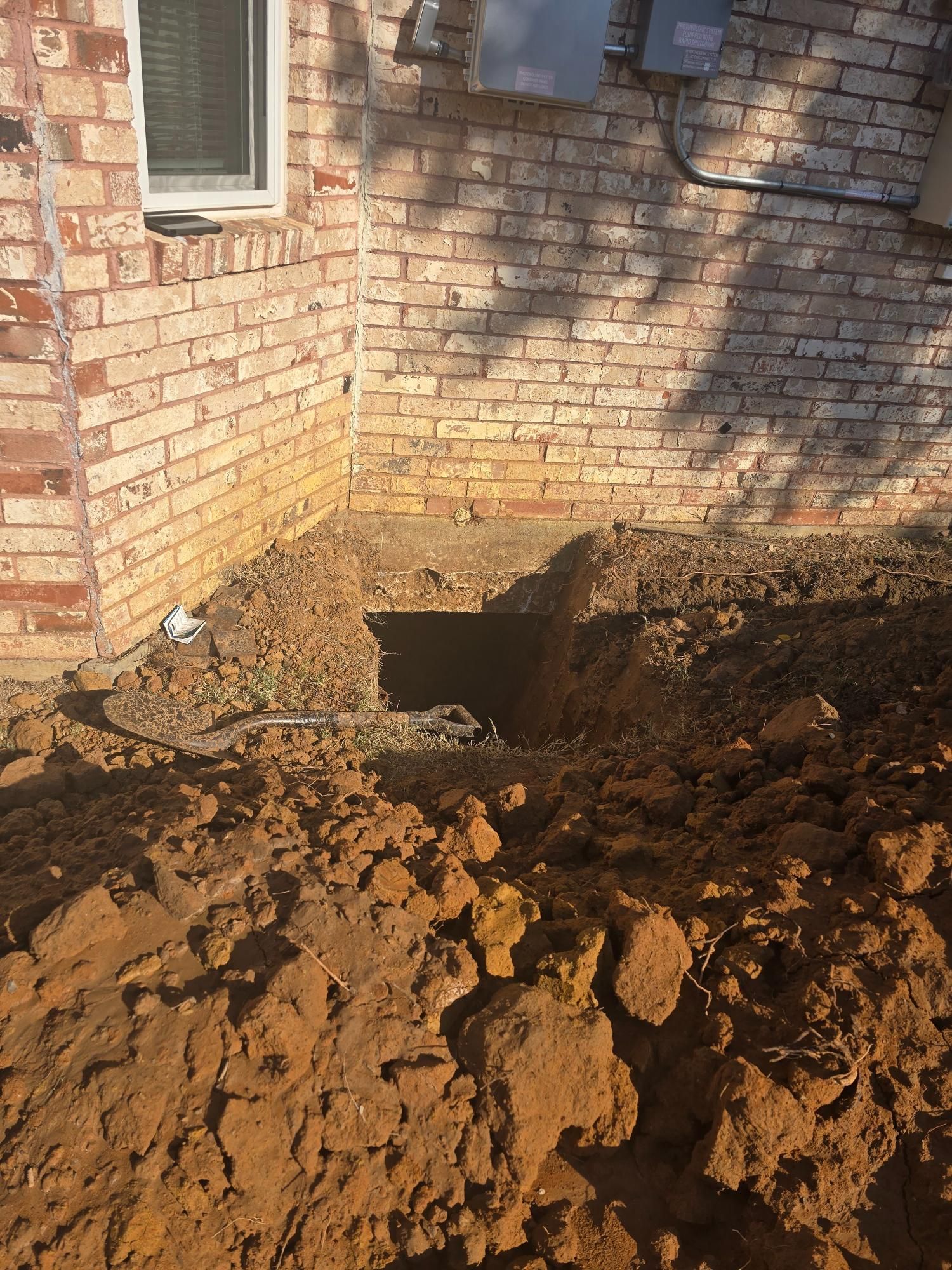 Hole dug next to a brick building's foundation, with dirt pile in foreground.