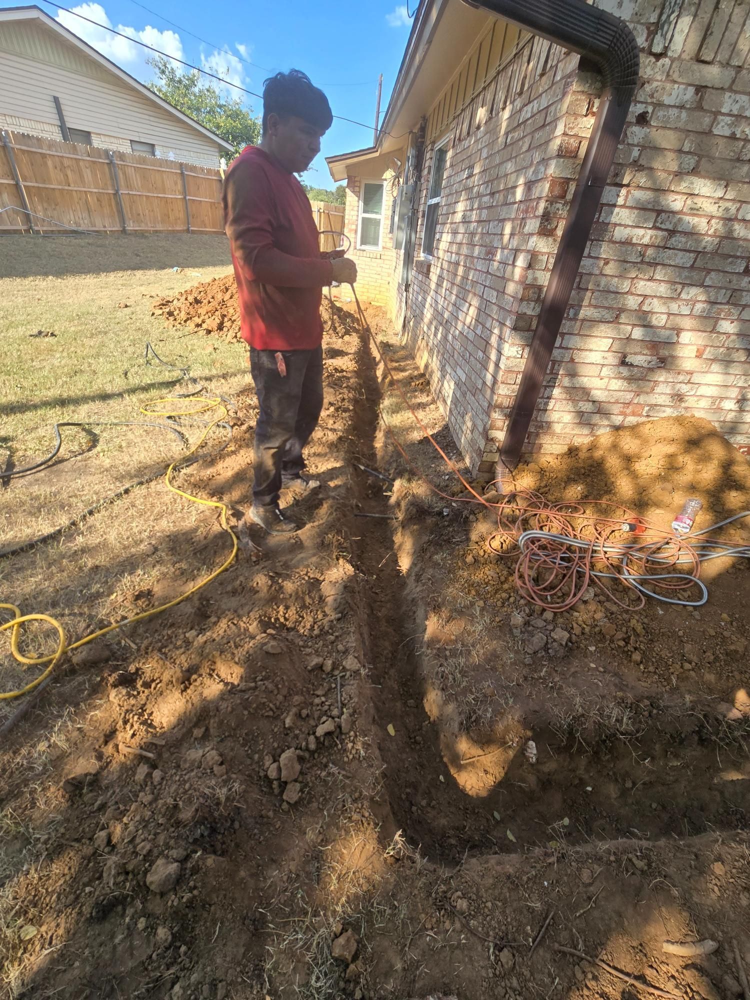 Person digging trench next to a brick building.