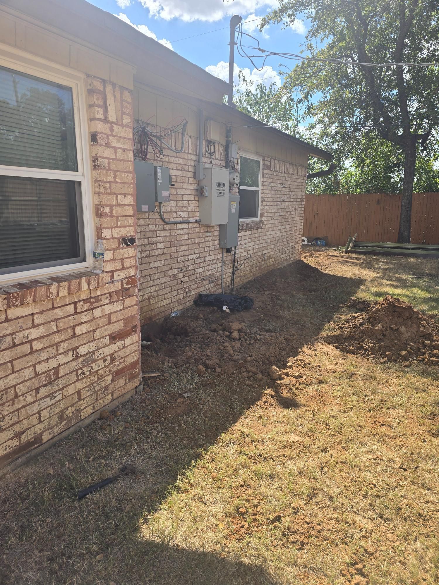 Brick building exterior with electrical boxes, a window, and dirt landscaping. Sunny day.
