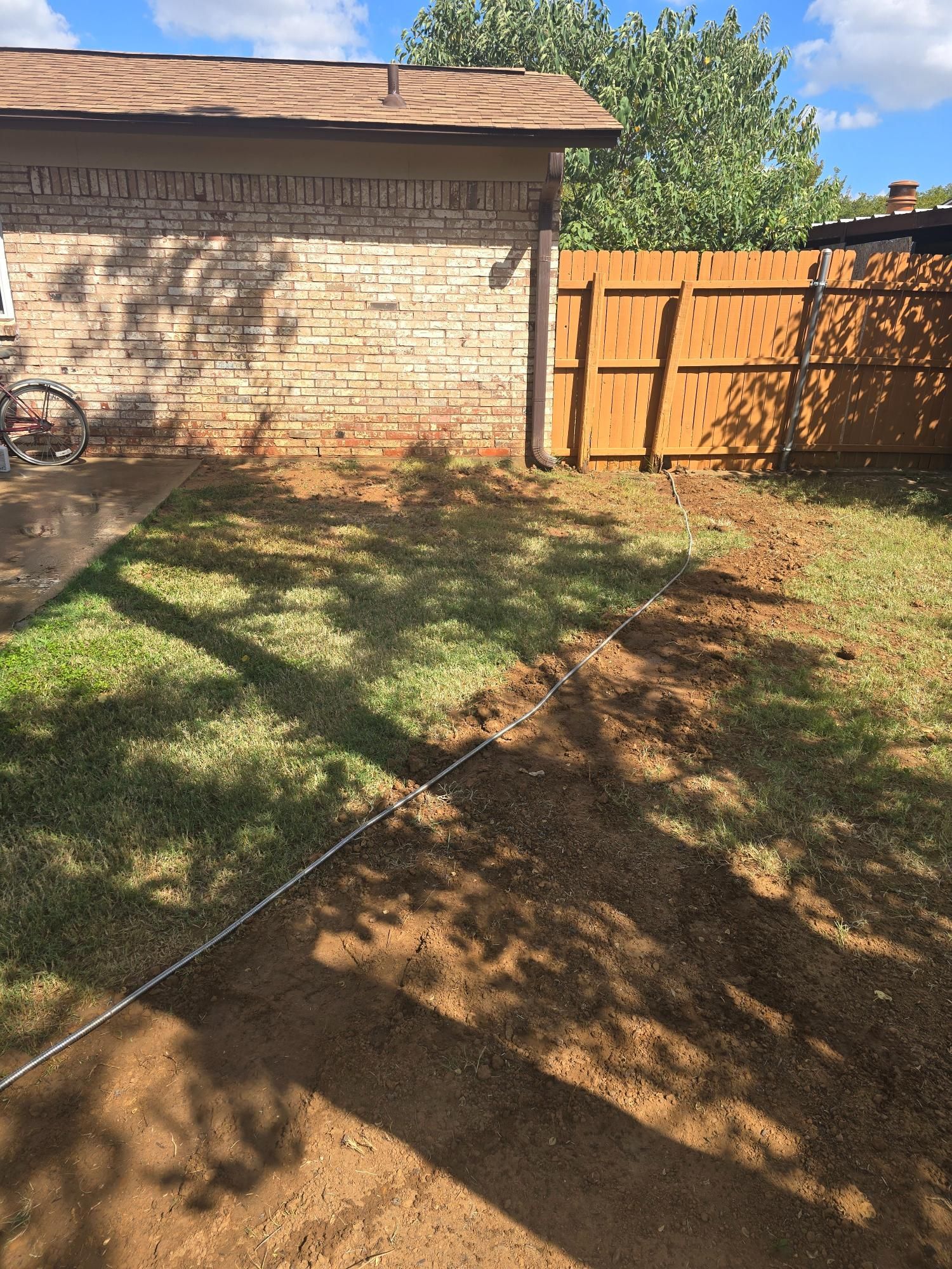 Backyard landscaping project with dirt path, brick wall, wooden fence, and green grass.
