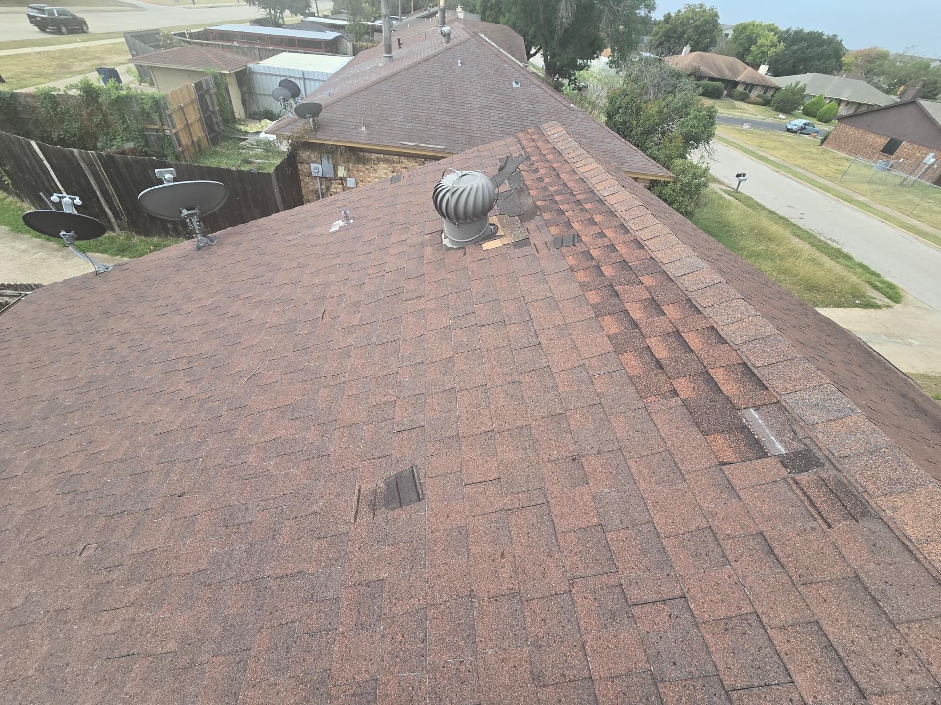 Brown shingled roof with a vent, viewed from above, houses in the background, daytime.