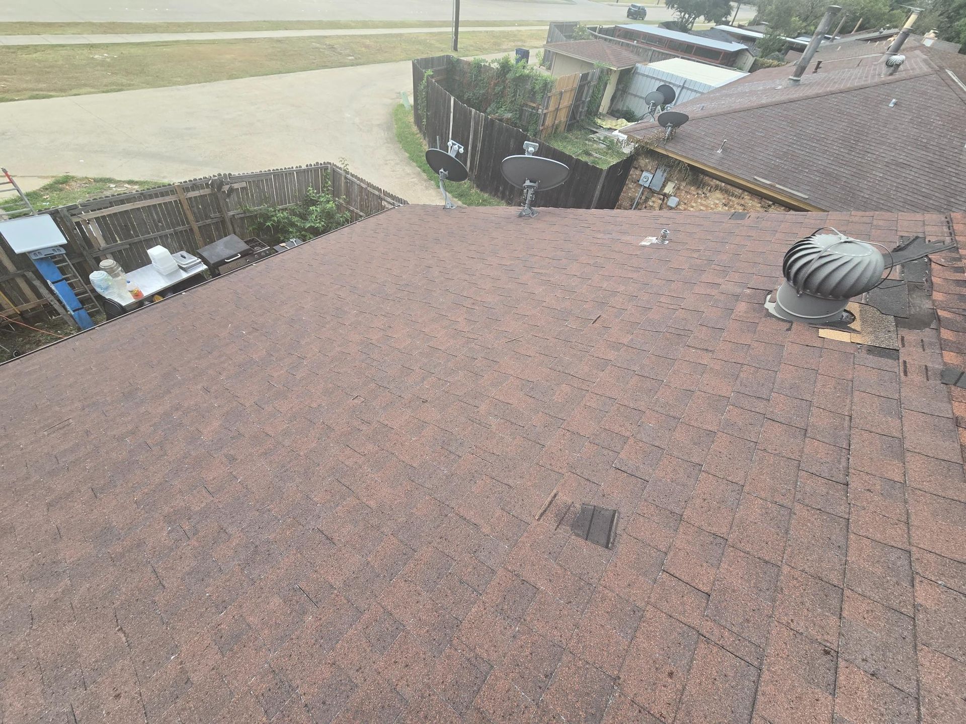 Brown asphalt shingle roof with a vent and surrounding neighborhood in the background.